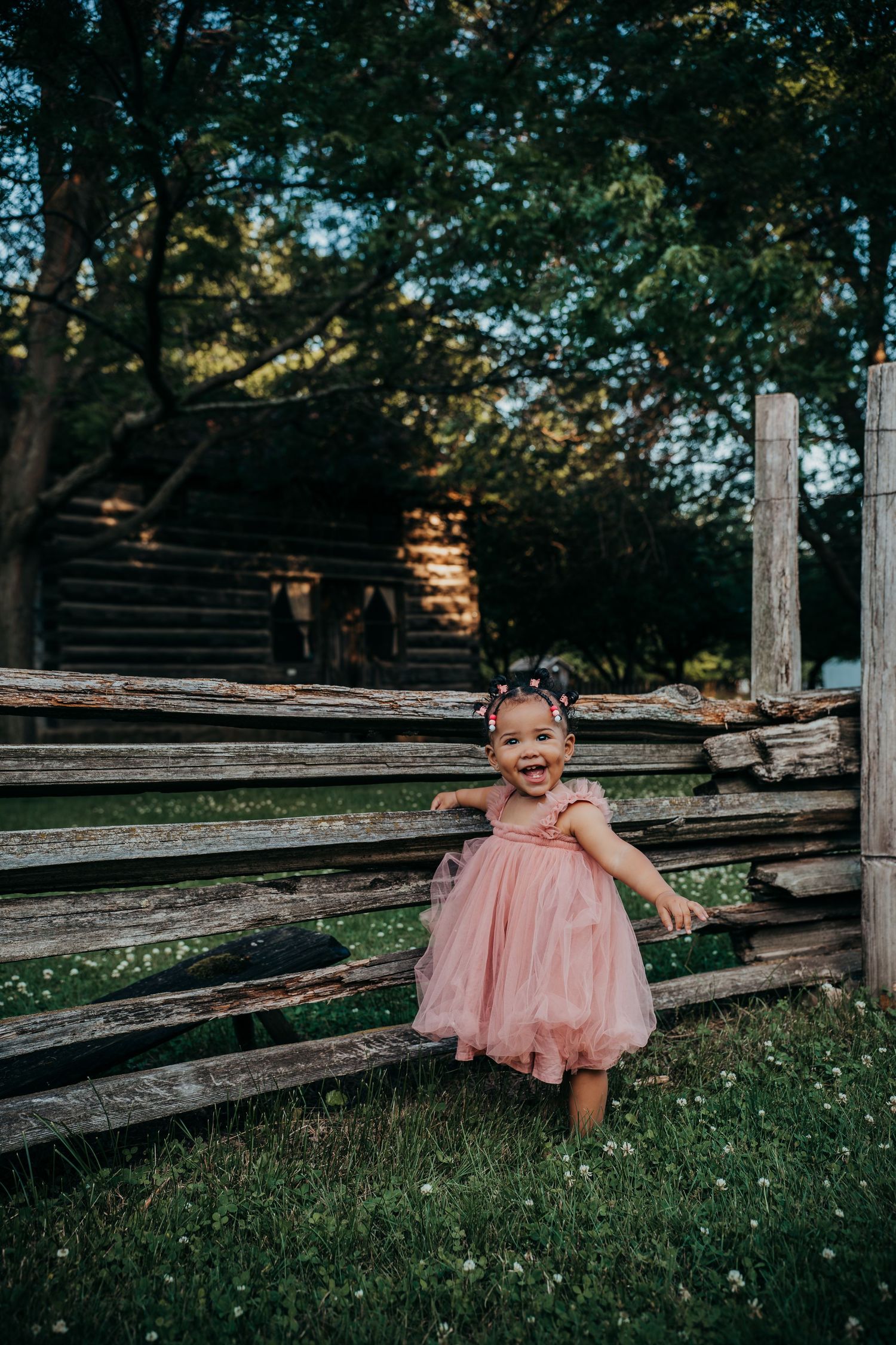 A child in a pink tulle dress plays joyfully on wooden benches in a sunny outdoor setting.