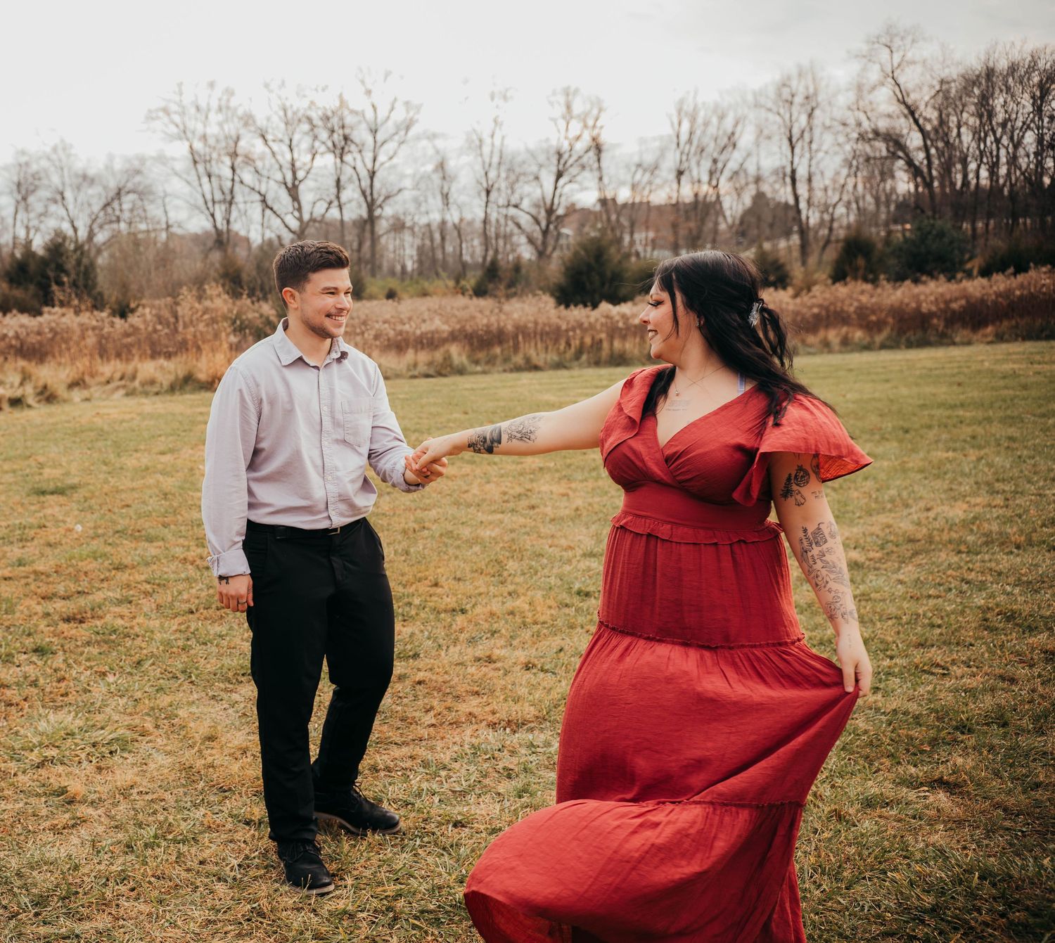 A couple dances together in a grassy field during autumn, with the person in red twirling their flowing dress.