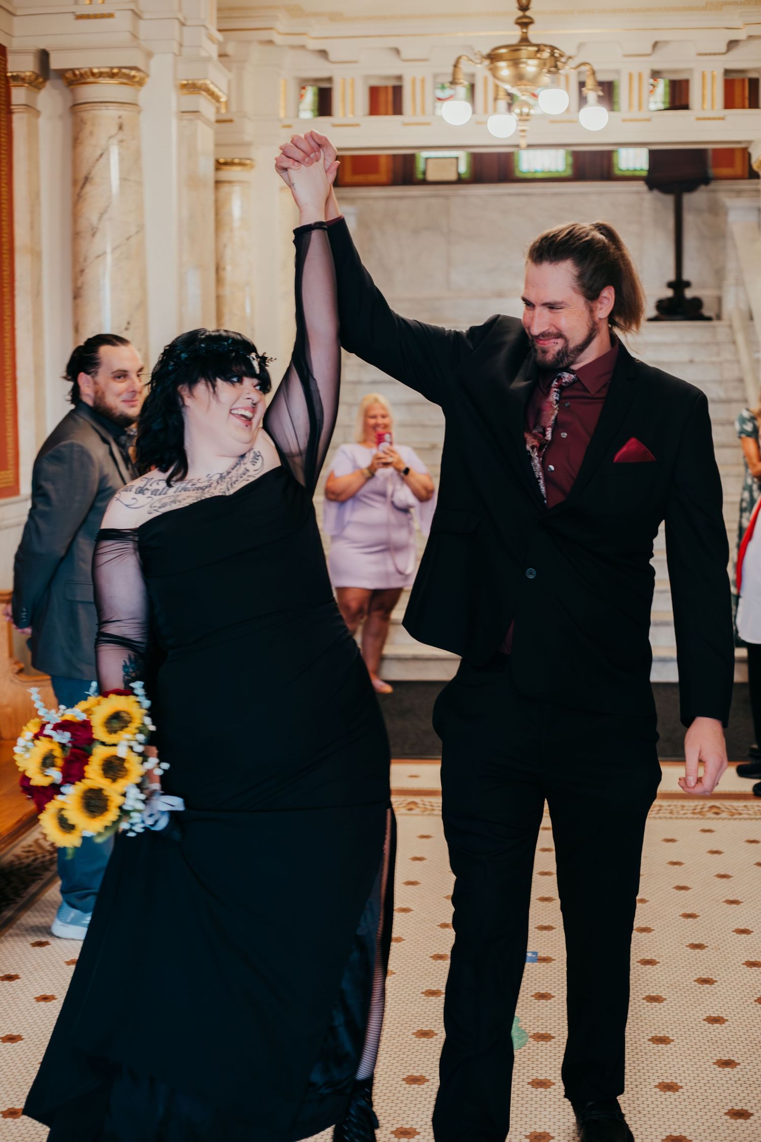 A couple in formal attire shares a romantic dance moment with sunflowers at an elegant indoor venue.