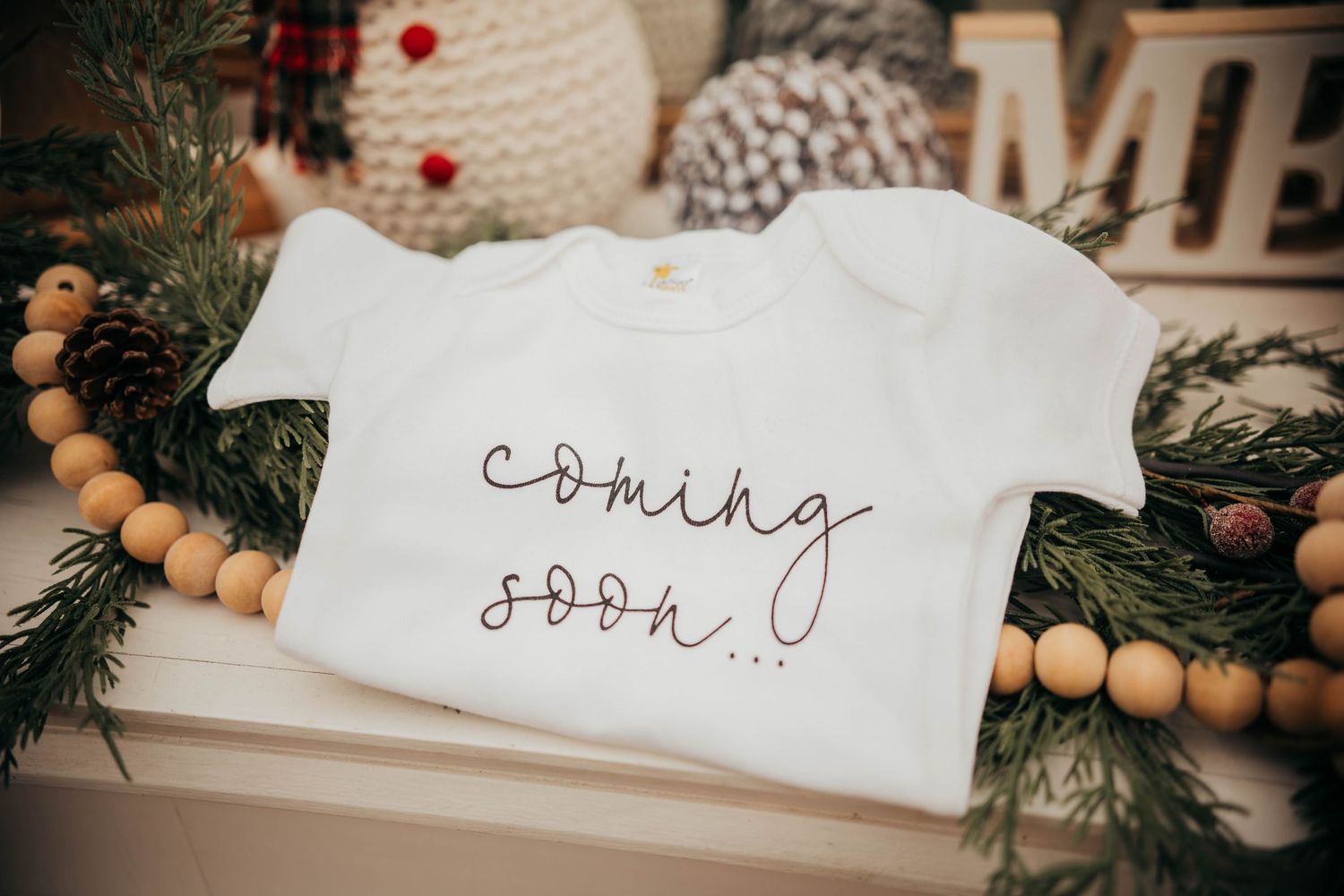 Handwritten calligraphy on white paper surrounded by wooden beads and evergreen branches creates a festive holiday display.