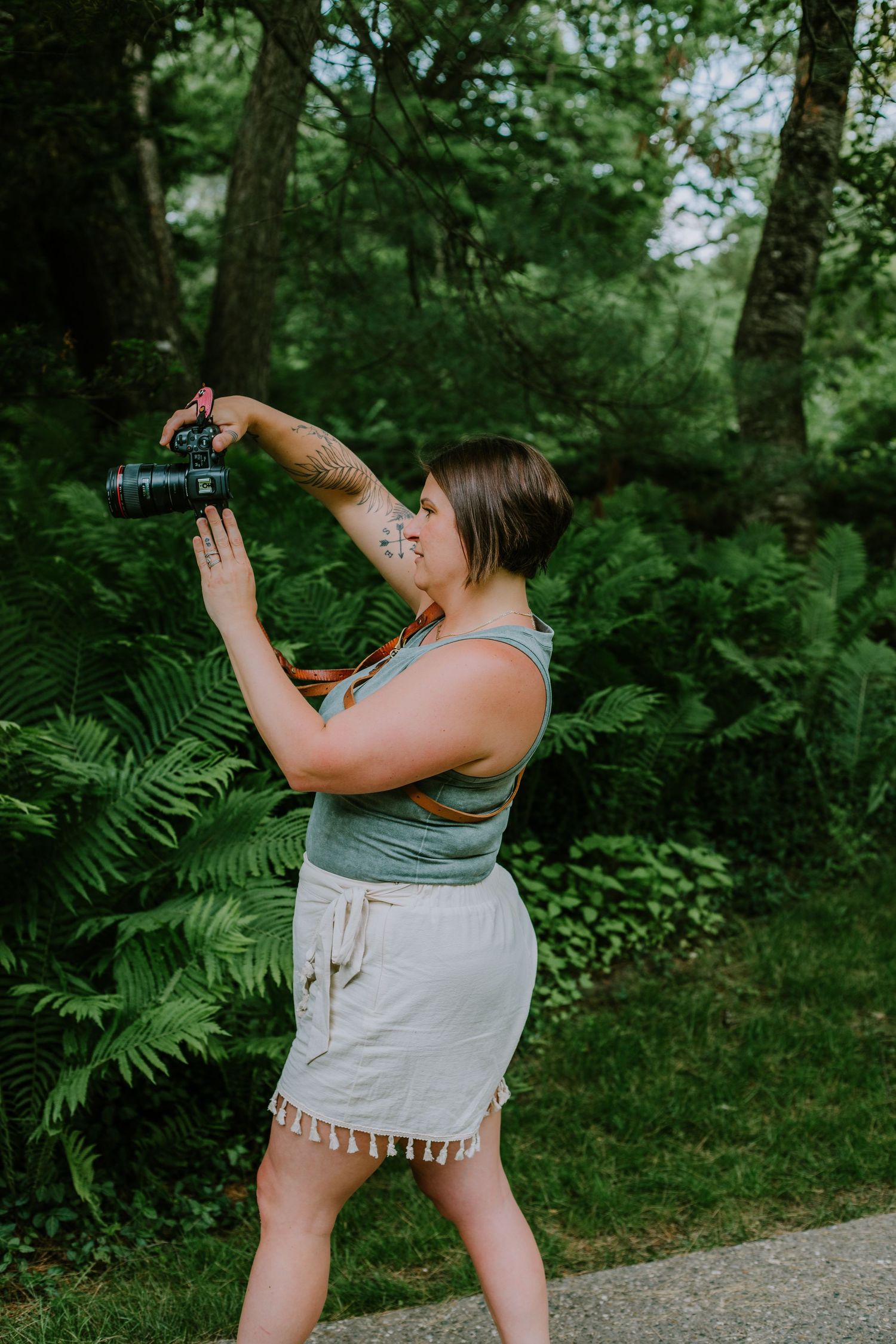 A photographer in a casual outfit takes pictures in a lush green forest setting.