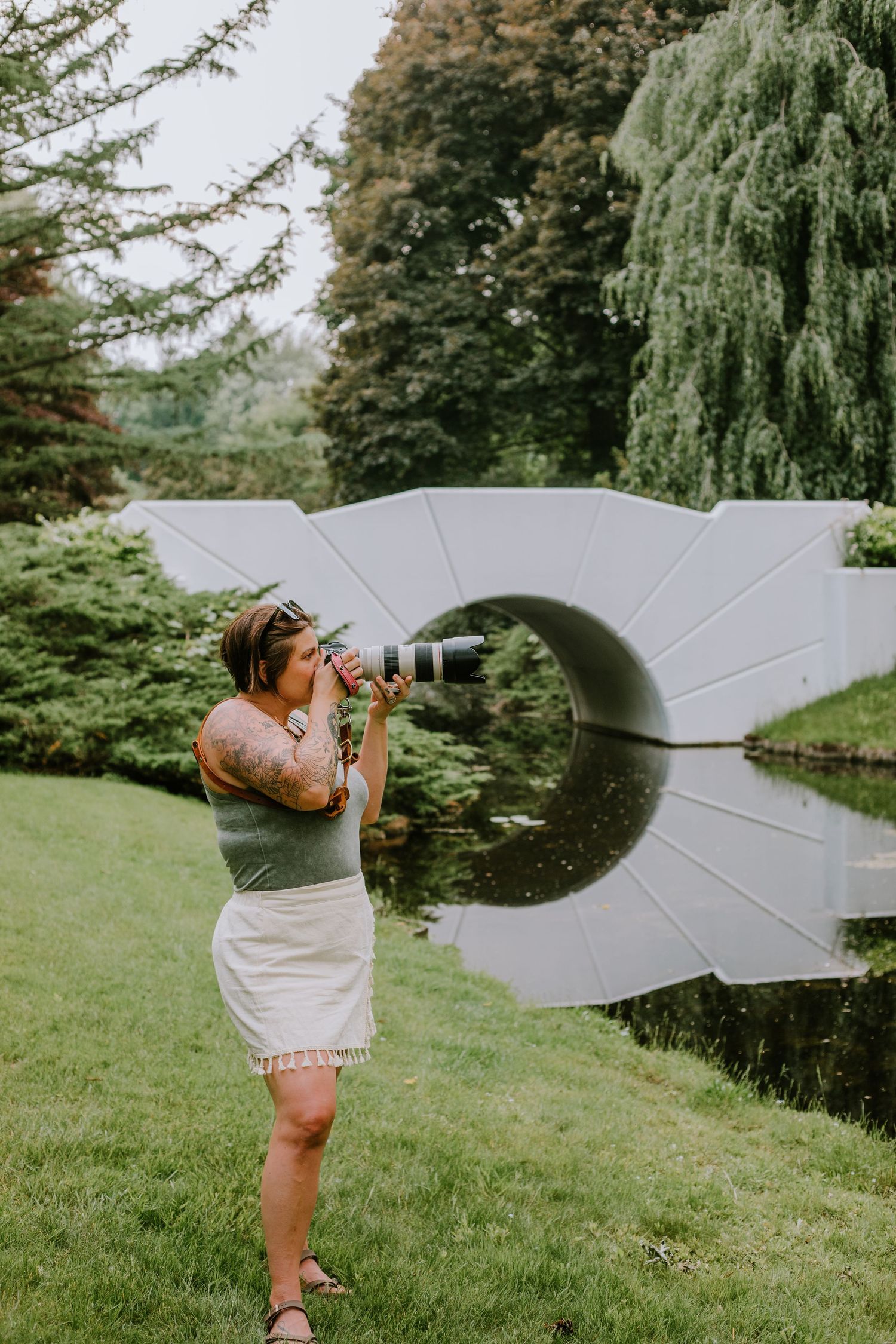 A photographer capturing images by a pond with modern solar panels visible in the background.