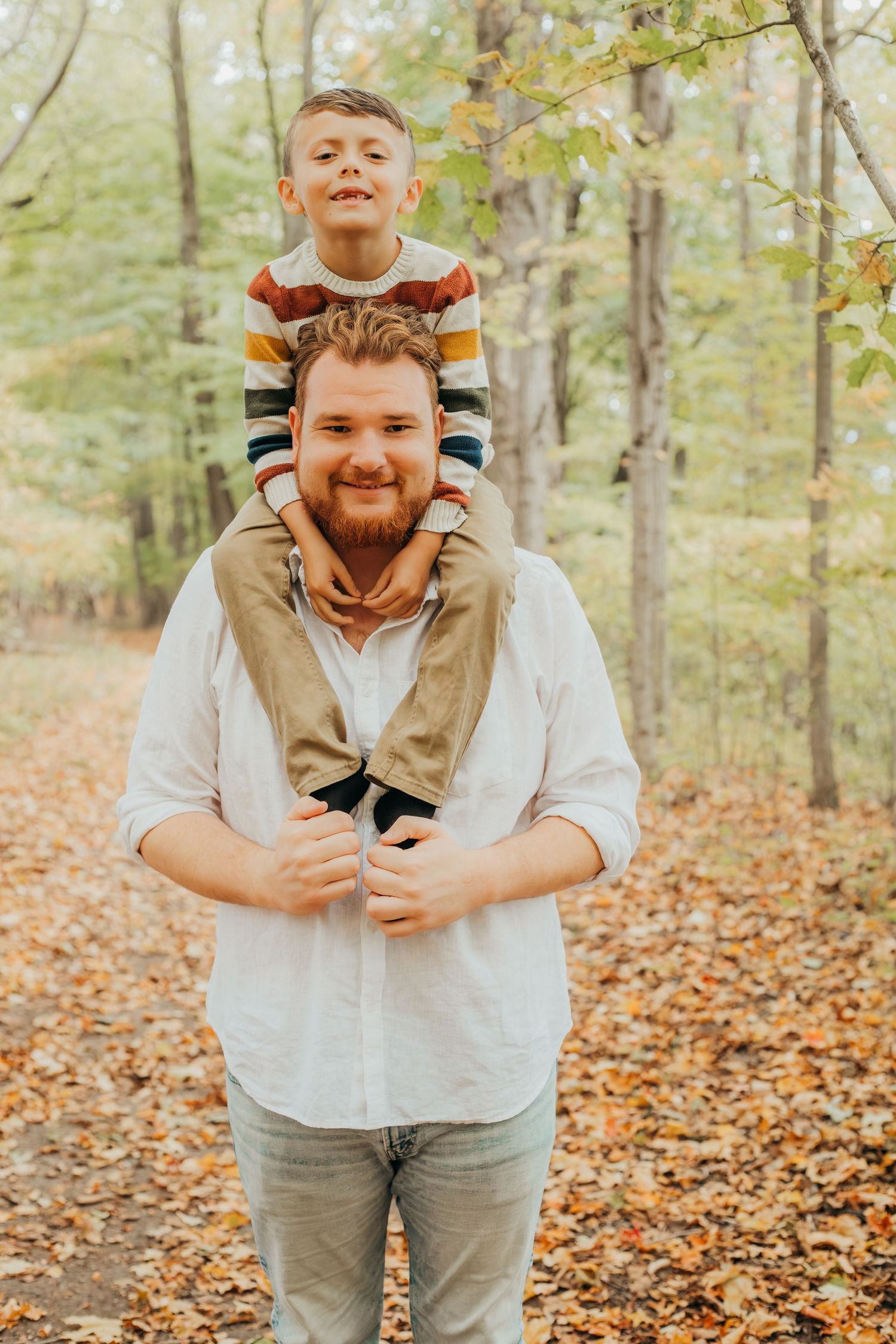 A joyful autumn family photoshoot in a forest with fallen leaves showing playful expressions and warm moments.