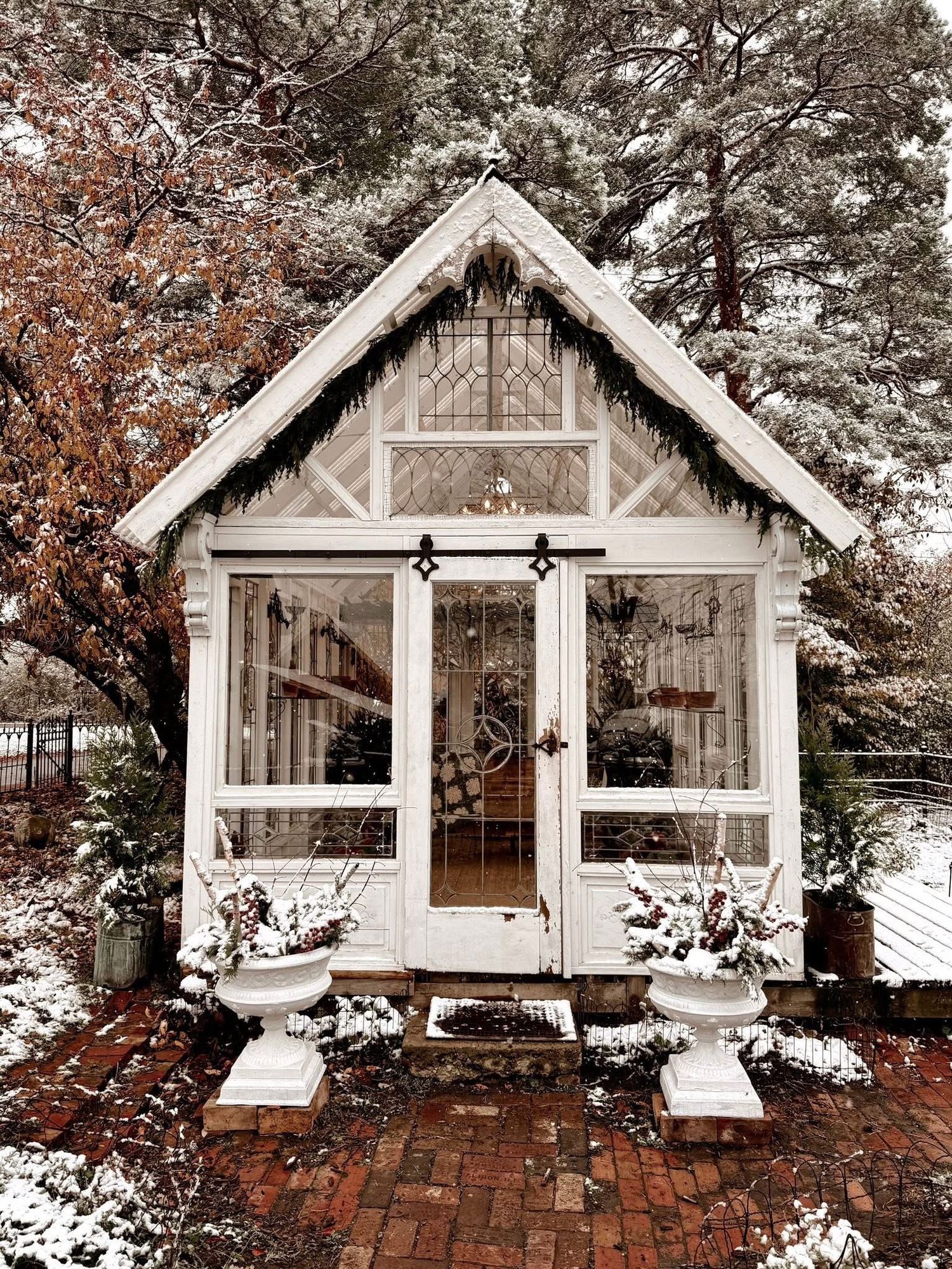 Panoramic view of a rustic white garden shed with brick walkway covered in snow during winter.