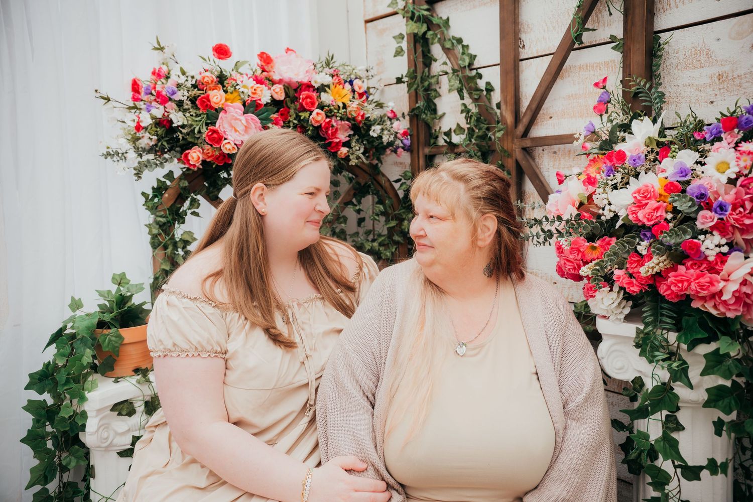 Two people share a joyful moment together surrounded by vibrant pink flowers and greenery in an outdoor setting.