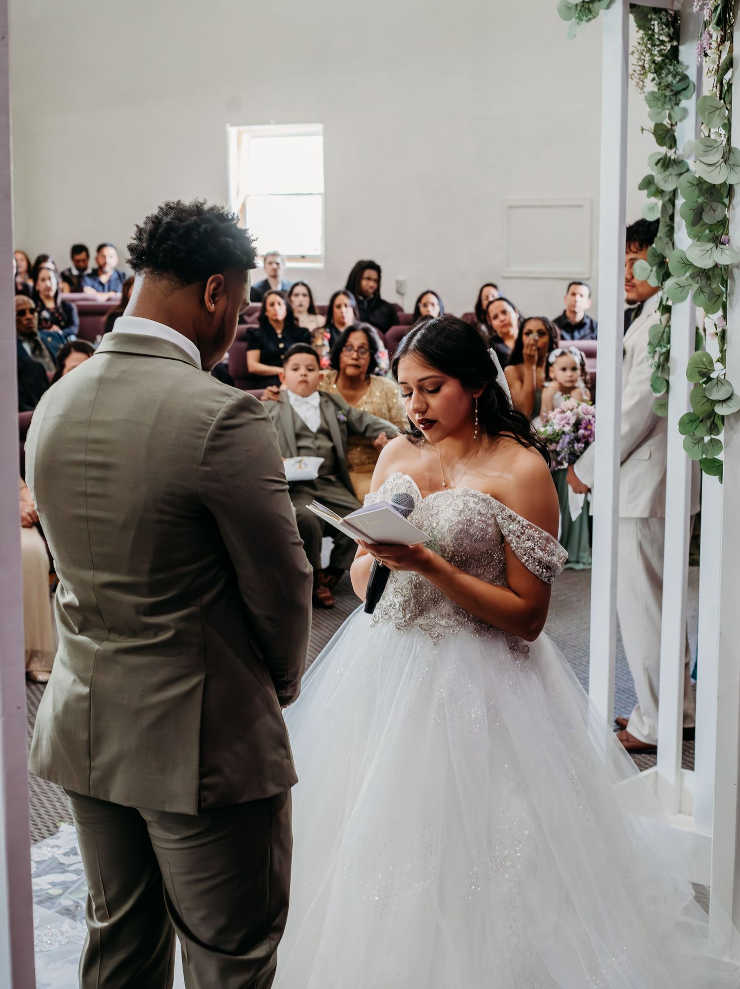 Newlyweds share their first dance together at a wedding reception surrounded by guests and decorative white pillars.