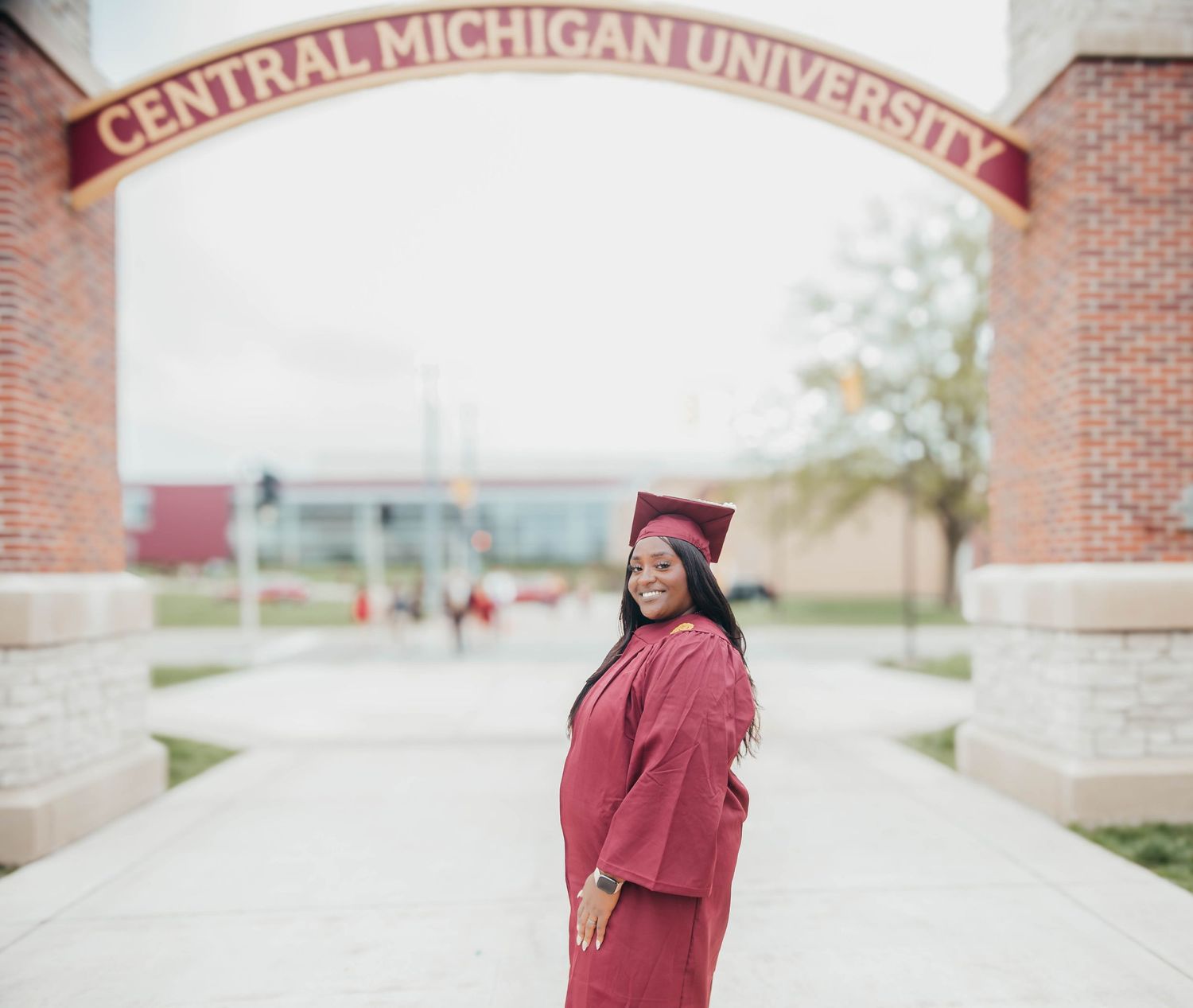 Graduate posing in maroon cap and gown on Central Michigan University campus during commencement celebrations.