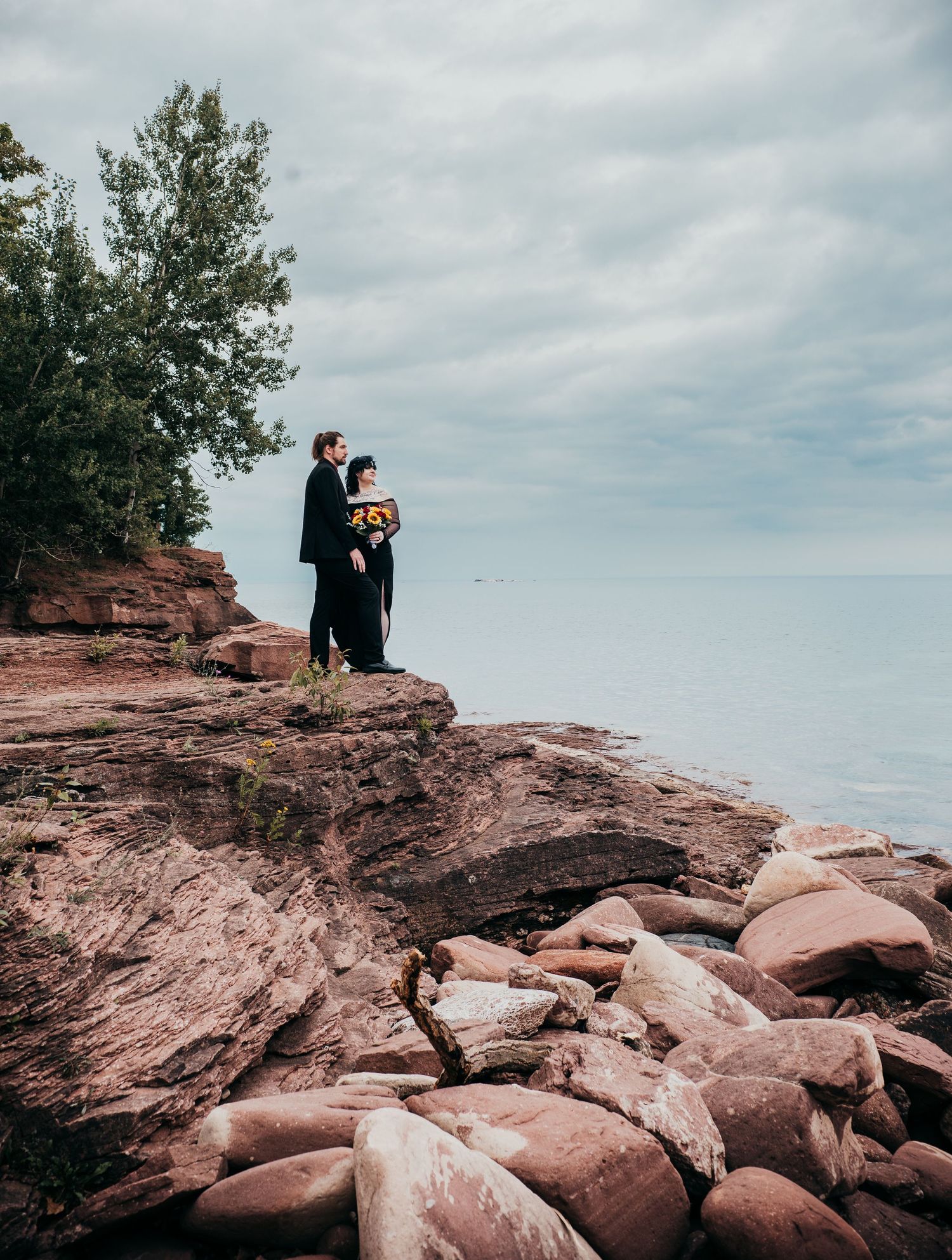 People sitting on red sandstone cliffs overlooking Lake Superior during a cloudy day at Presque Isle Park.