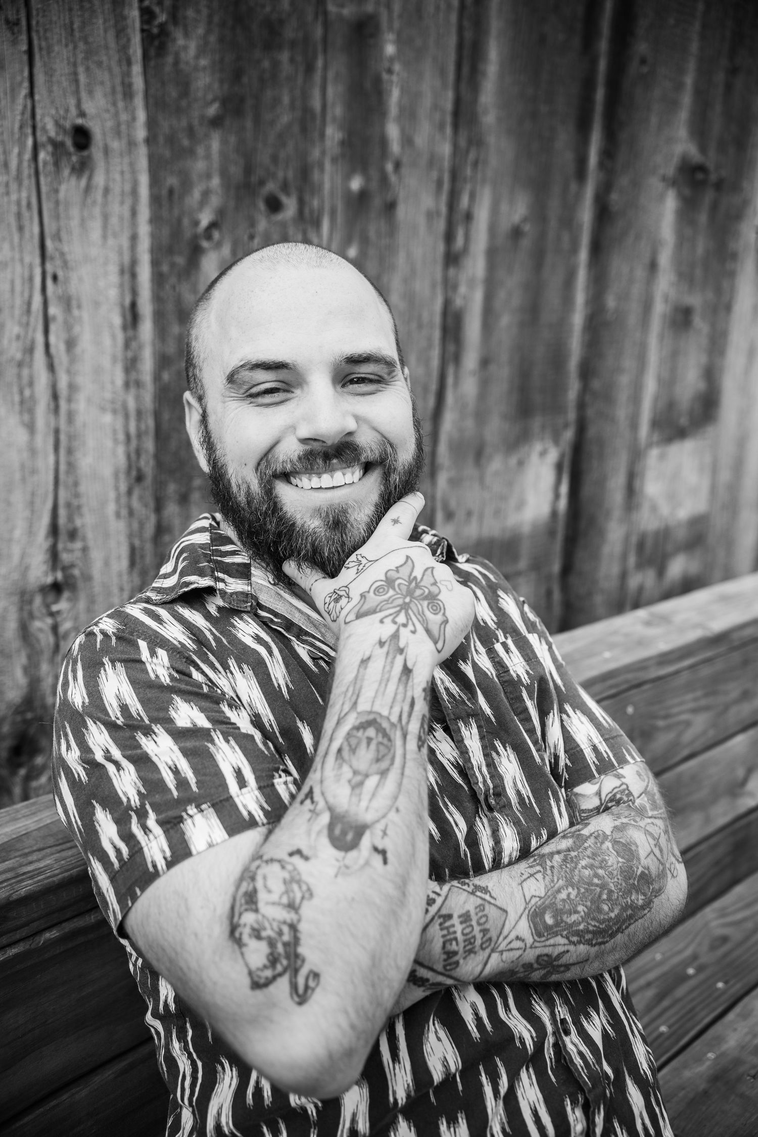 Black and white photo series showing a person with a beard and tattoos smiling and laughing against a wooden wall.