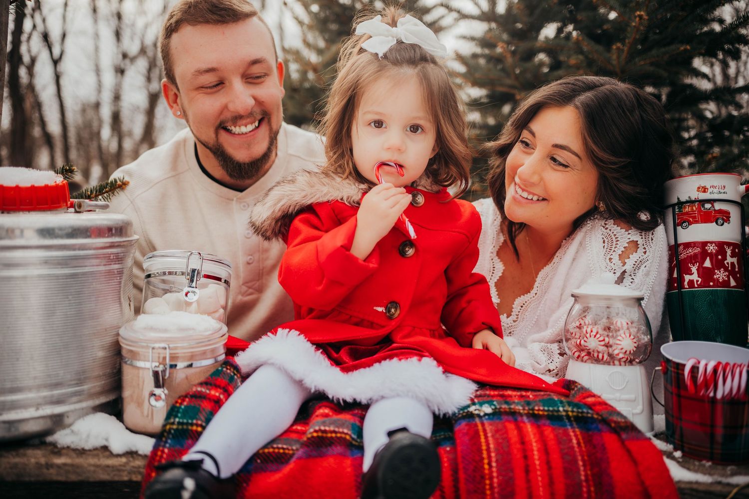 A family shares a festive moment on a plaid blanket surrounded by Christmas decorations and milk jugs in winter.