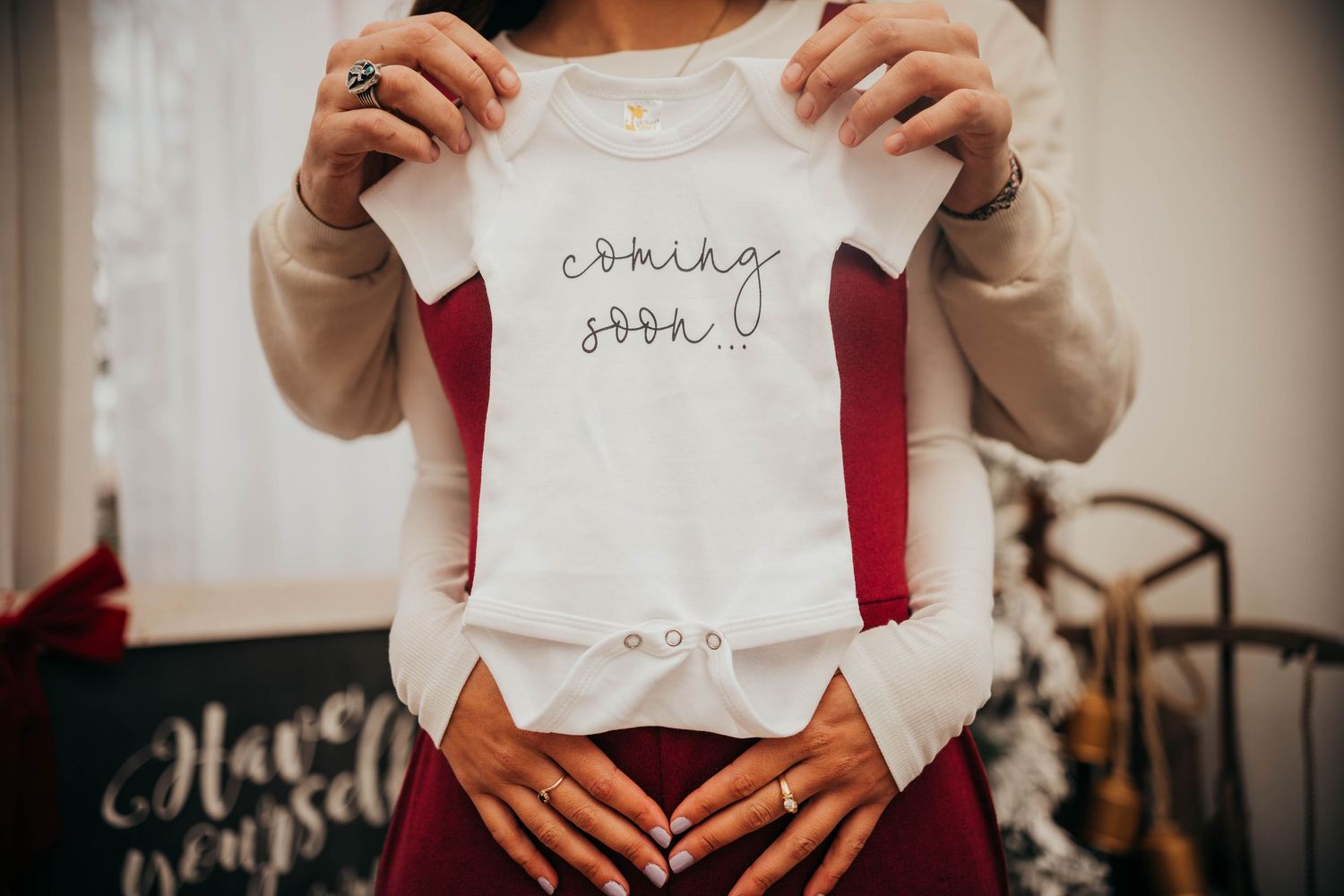 Someone holds up a white baby onesie with handwritten text against a burgundy background.