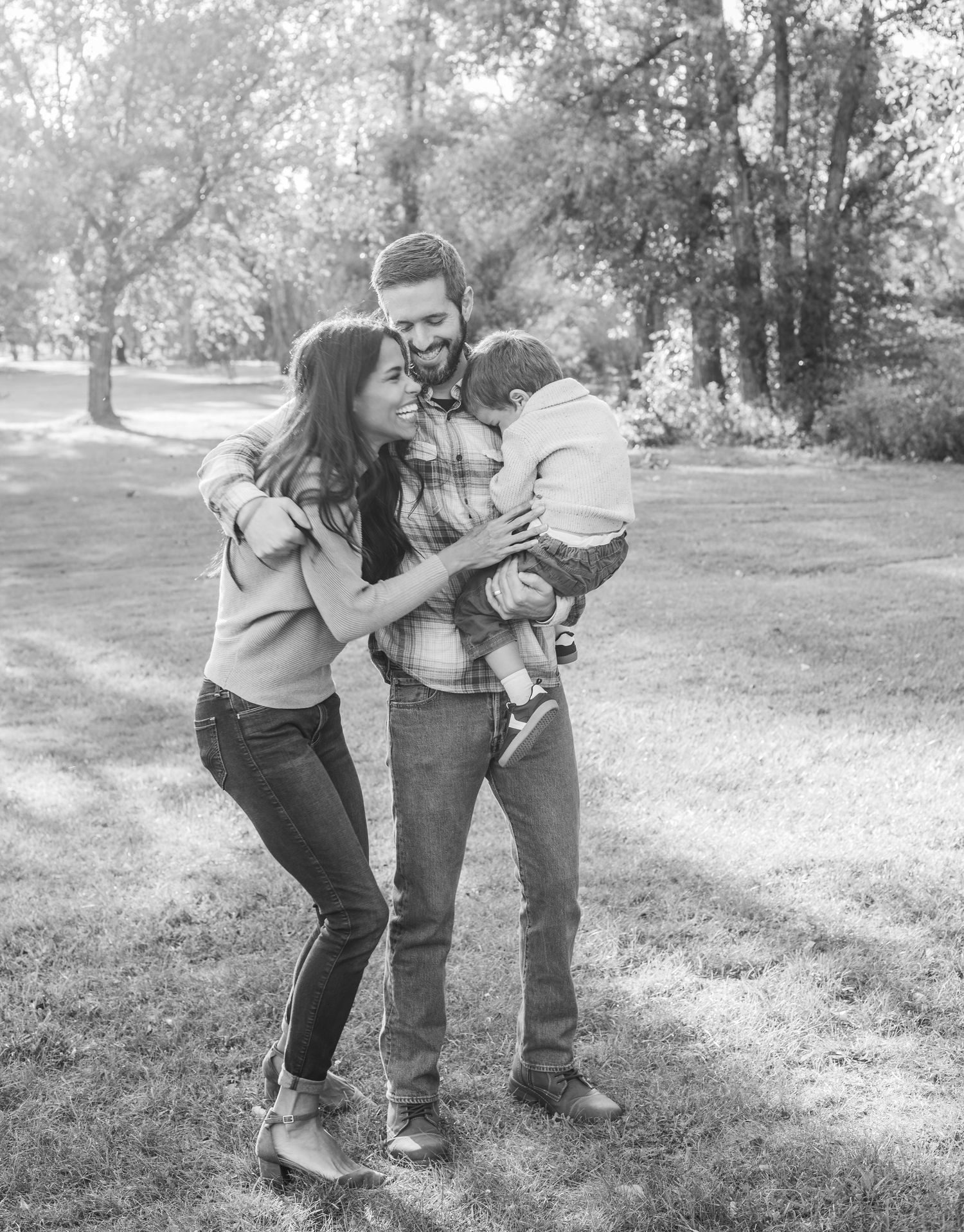 A loving family shares a joyful moment together outdoors in a park setting, captured in black and white.