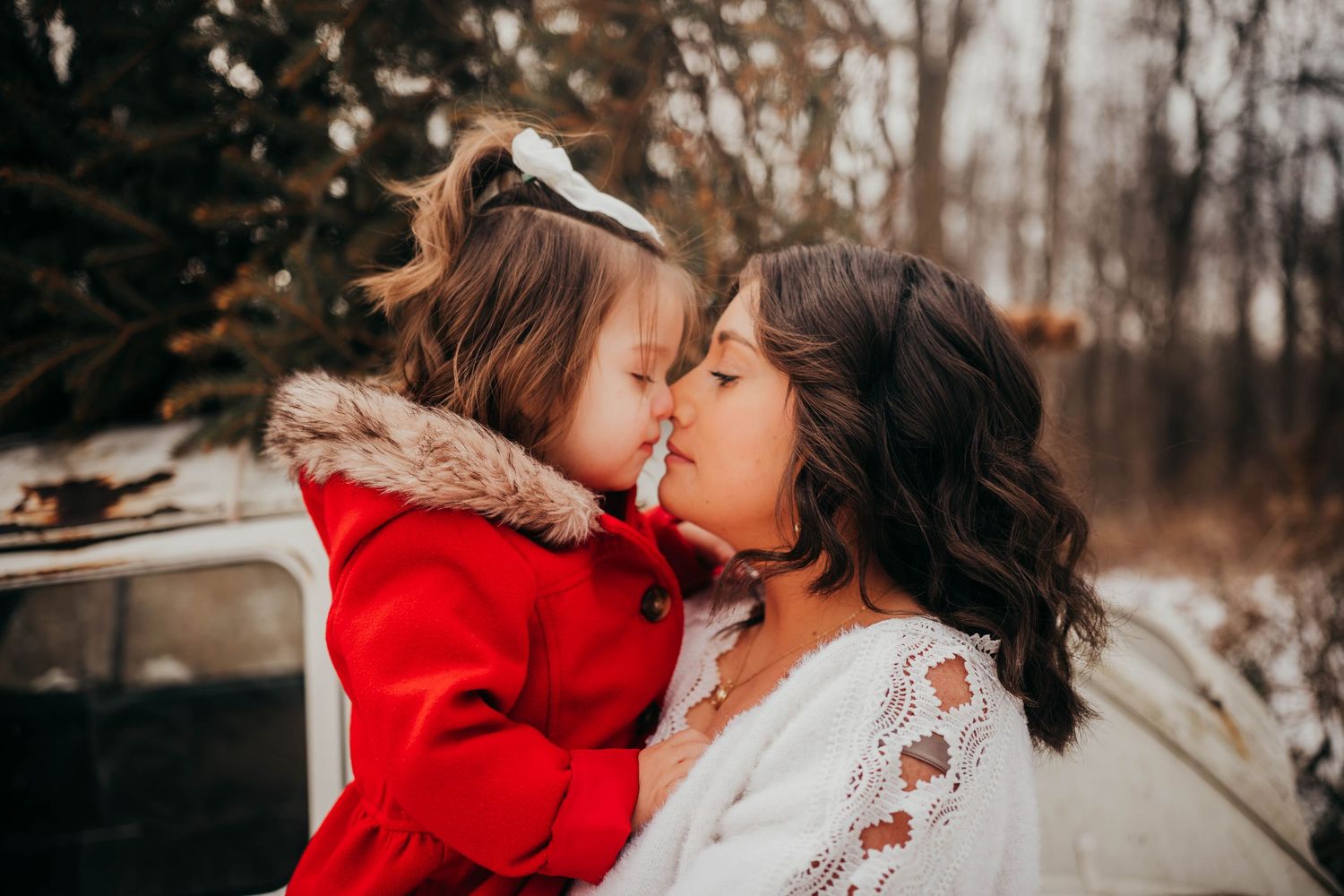 A tender winter moment shared between two people in red and white outfits against a snowy forest backdrop.
