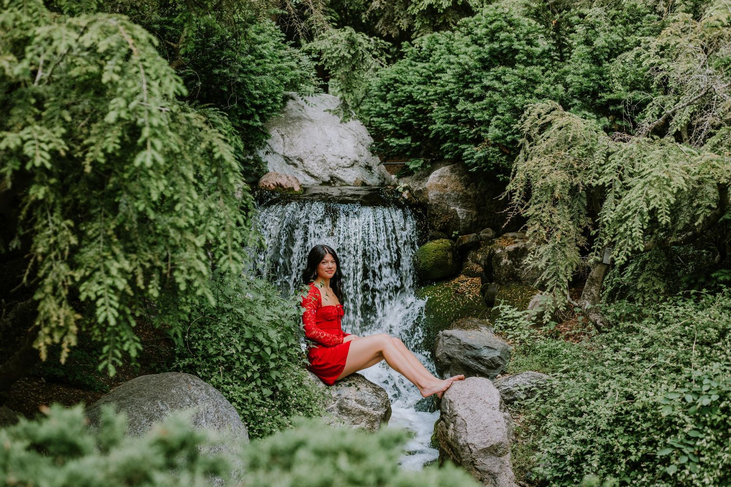 A couple explores a scenic waterfall trail surrounded by lush green forest and moss-covered rocks.