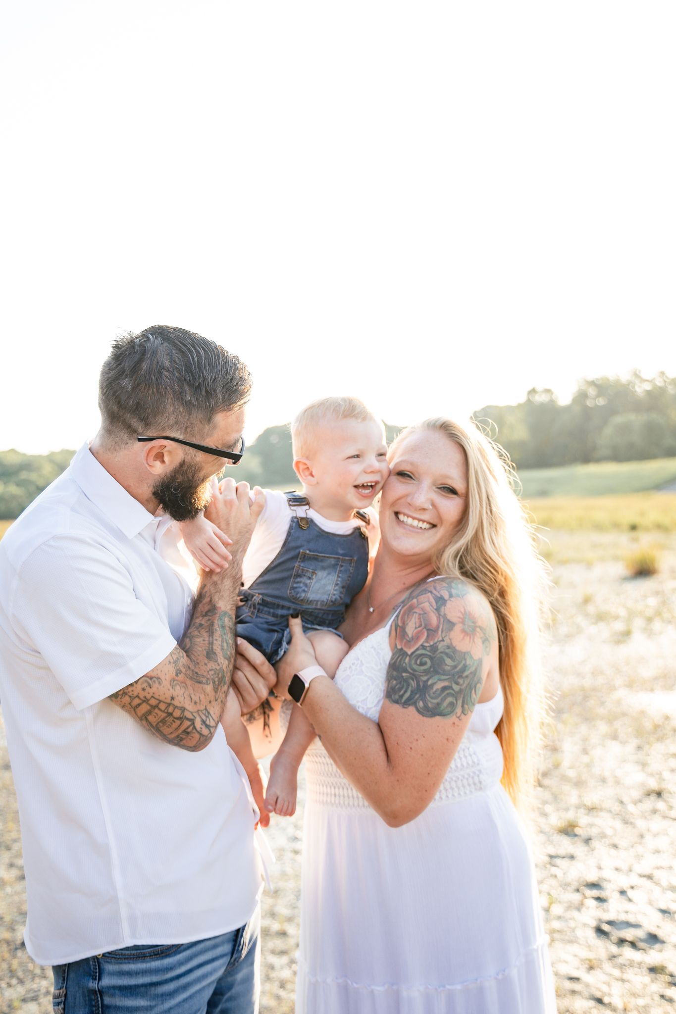 light and airy photo of a family smiling with their young son laughing standing in a field.