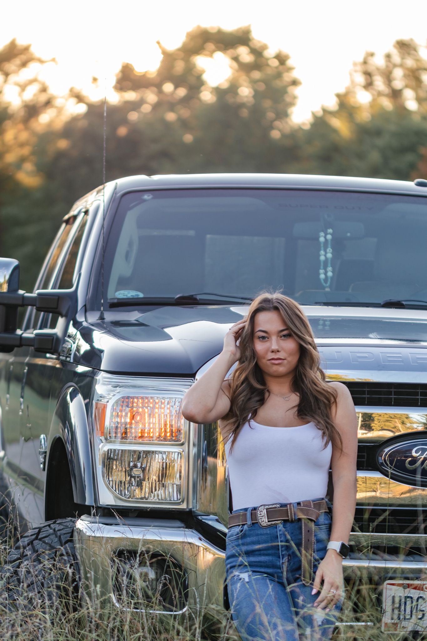 light and airy photo of a senior girl in front of a truck in a field.