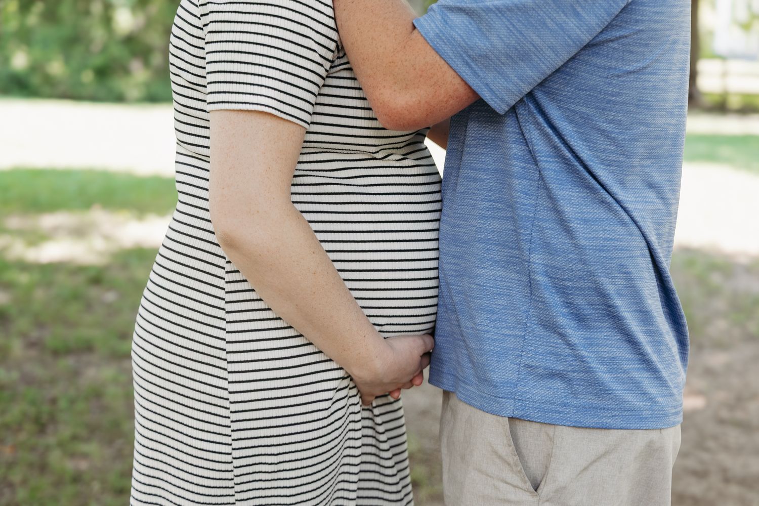 light and airy photo of a pregnant couple standing in a field holding her belly.