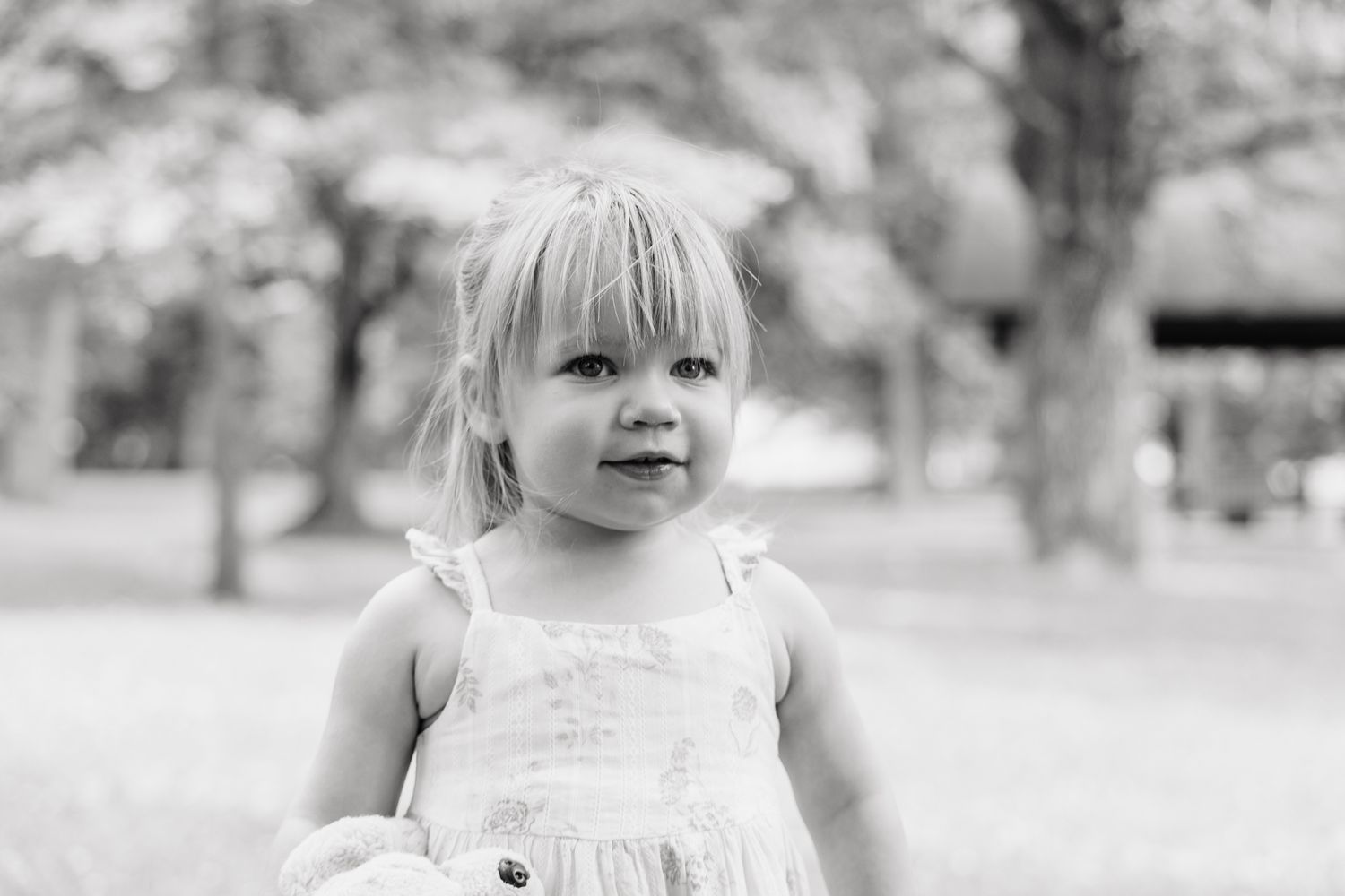 black and white photo of a young girl holding her stuffed dog looking at the camera