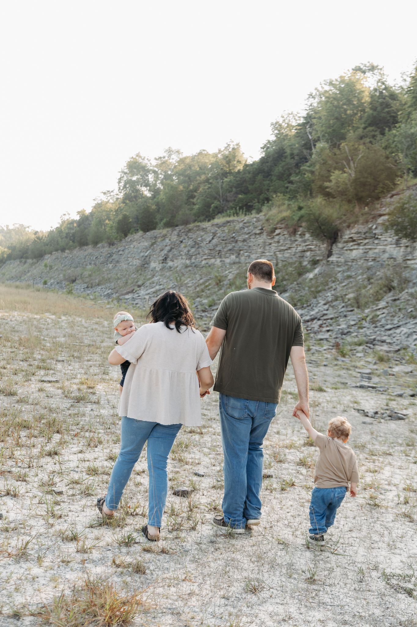 light and airy photo of a family with their two young children walking away from the camera in a rock spillway