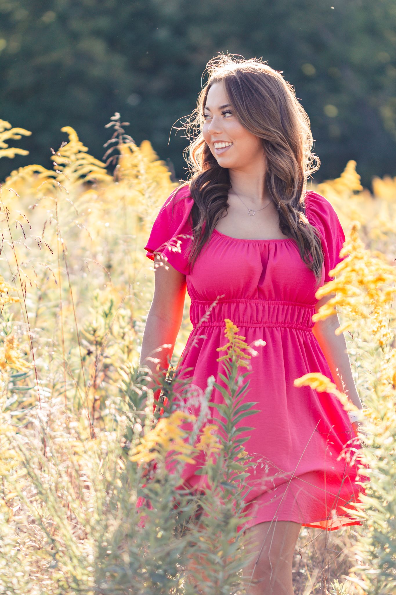 light and airy photo of a senior girl laughing in a field in a pink flowy dress