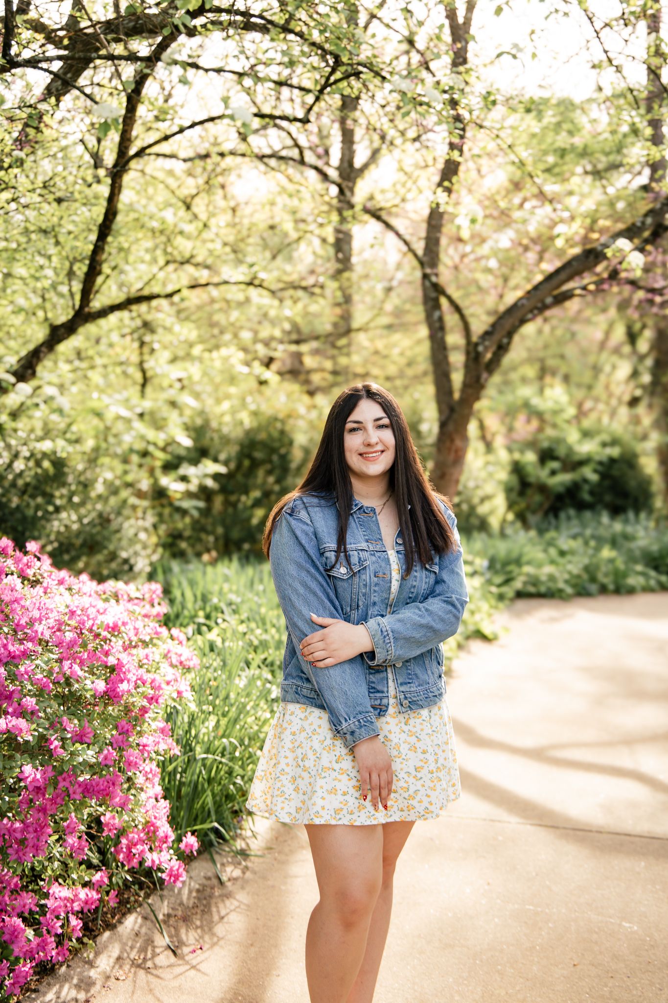 light and airy photo of a senior girl in a park standing next to bright pink flowers