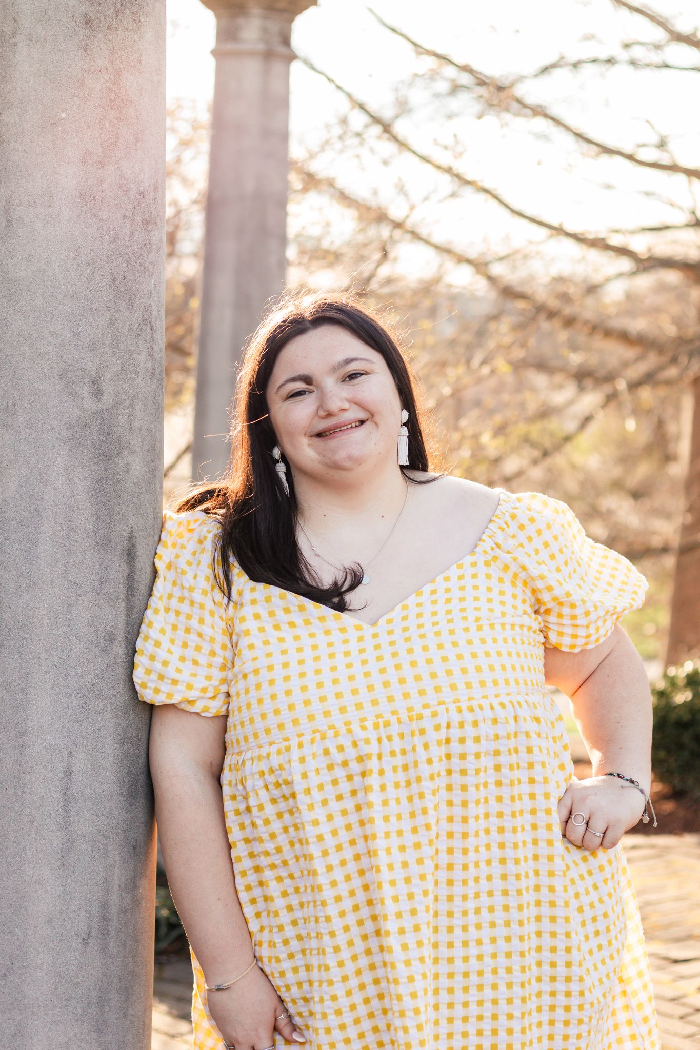 light and airy photo of a senior girl smiling leaning up against a cement pole