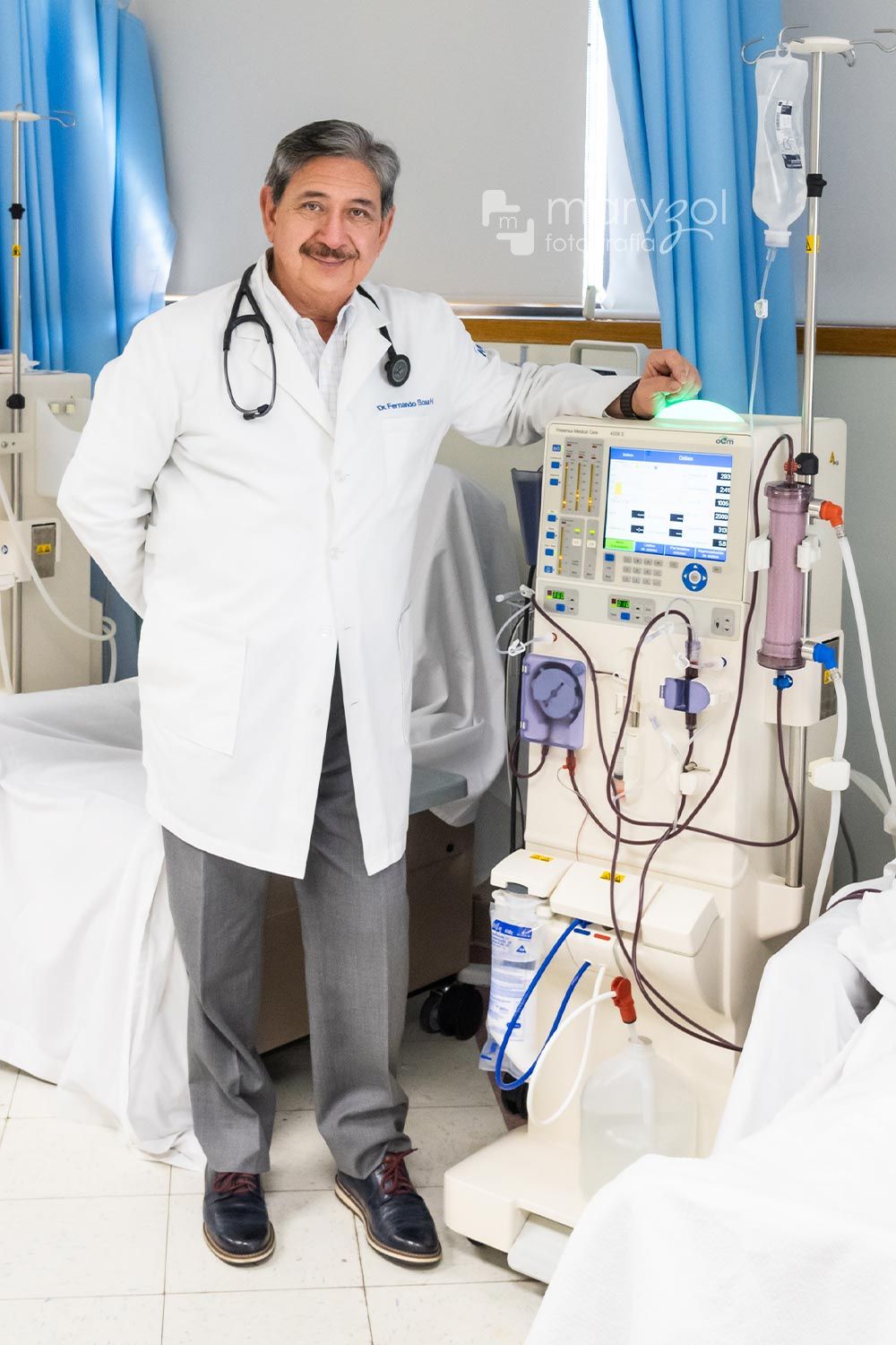 Doctor sonriendo de pie a lado de una máquina de hemodiálisis.
