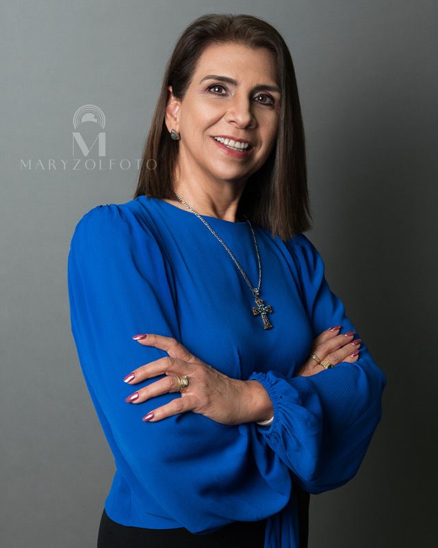 Retrato de mujer de negocios sonriendo y con los brazos cruzados, usando blusa azul.