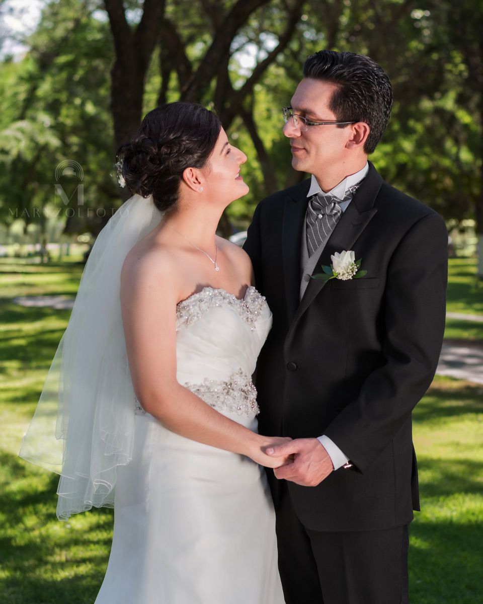 Pareja de recién casados en un parque, se toman de la mano y se miran a los ojos.