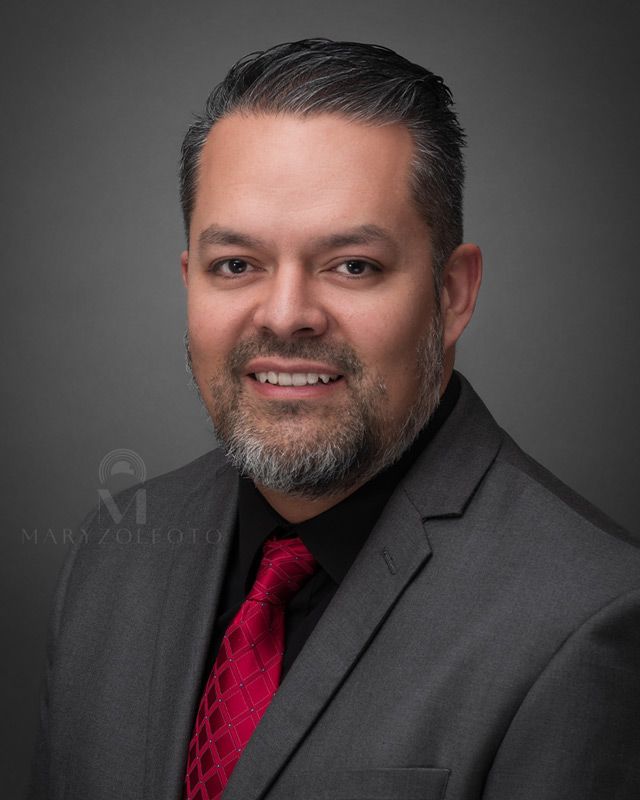 Retrato de estudio de hombre de negocios sonriendo, usando traje gris, camisa negra y corbata roja.