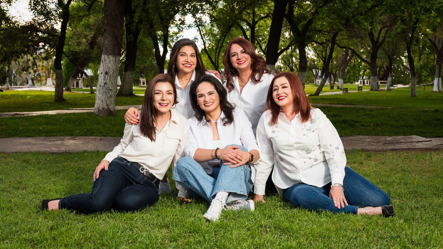 Grupo de cinco amigas felices sentadas sobre el césped de un parque.