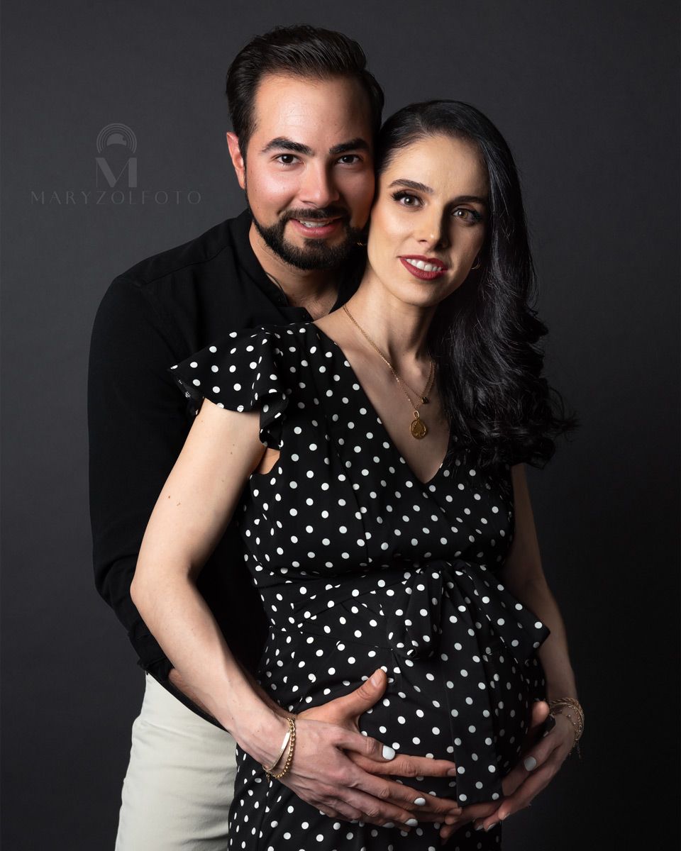 Retrato de estudio de pareja hombre y mujer. Ella está embarazada y él está detrás de ella tomando con sus manos su vientre.