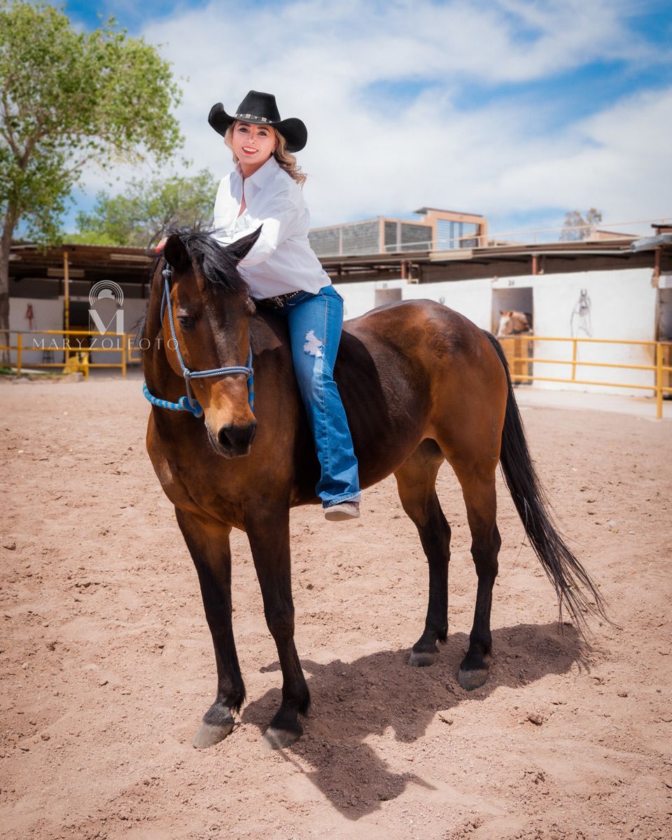 Mujer vaquera usando tejana, jeans y camisa blanca cabalgando un caballo café.