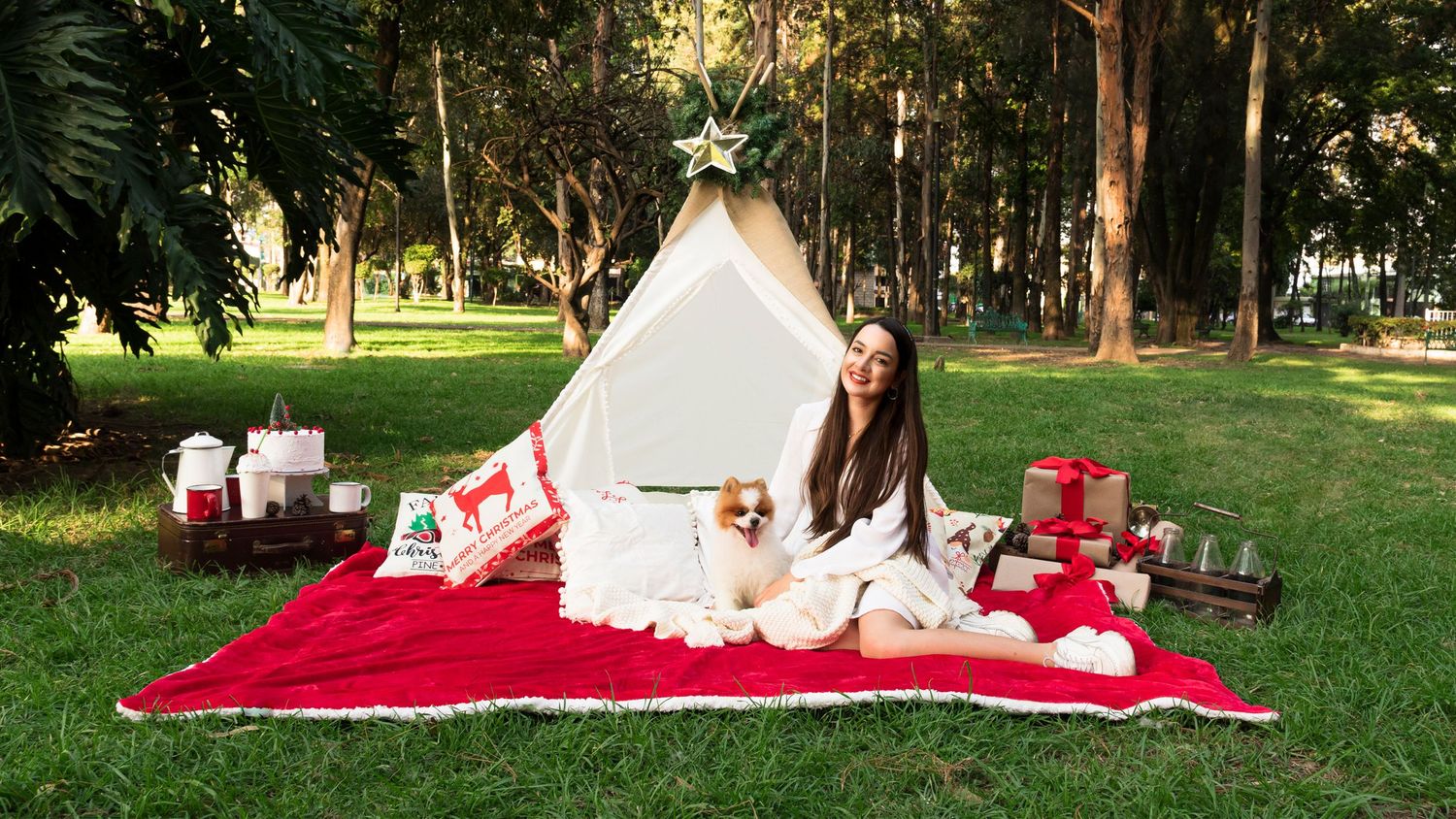 Mujer joven disfrutando de un picnic navideño en el parque con su perro Pomeranian. Detrás de ellos hay un teepee.