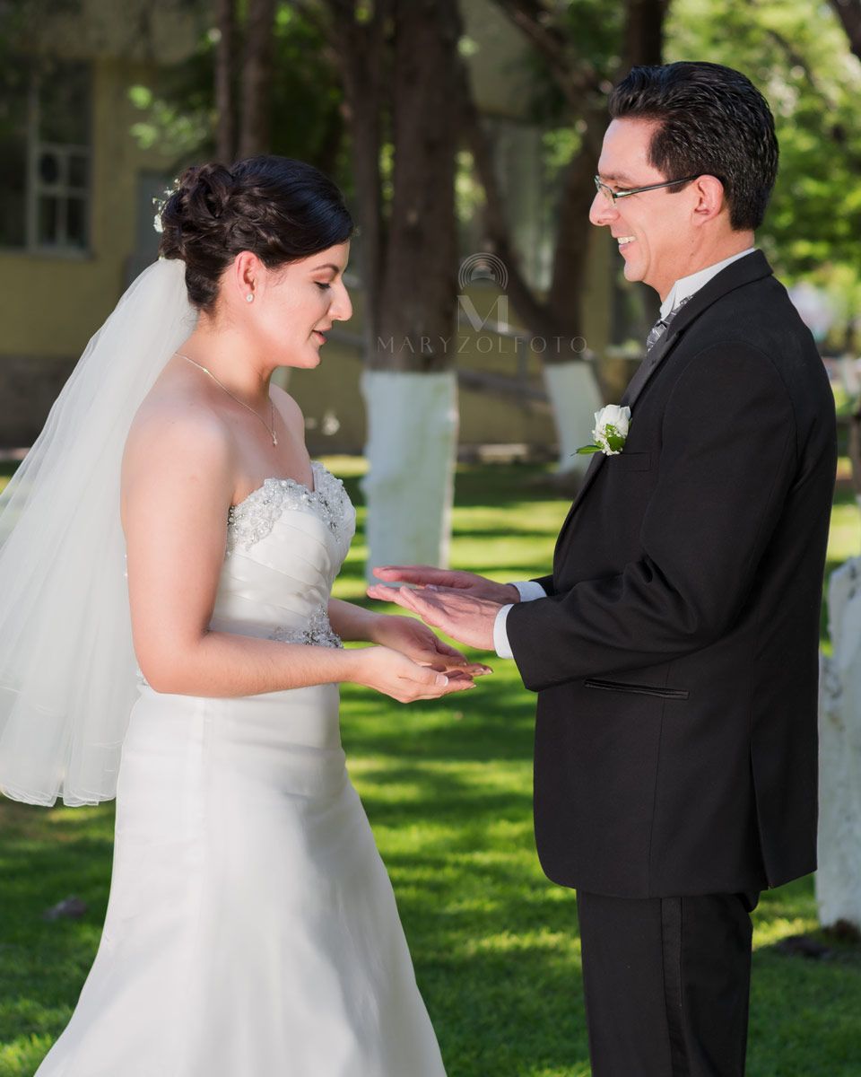 Pareja de recién casados en un parque, están de pie uno frente al otro y haciendo juegos con sus manos.