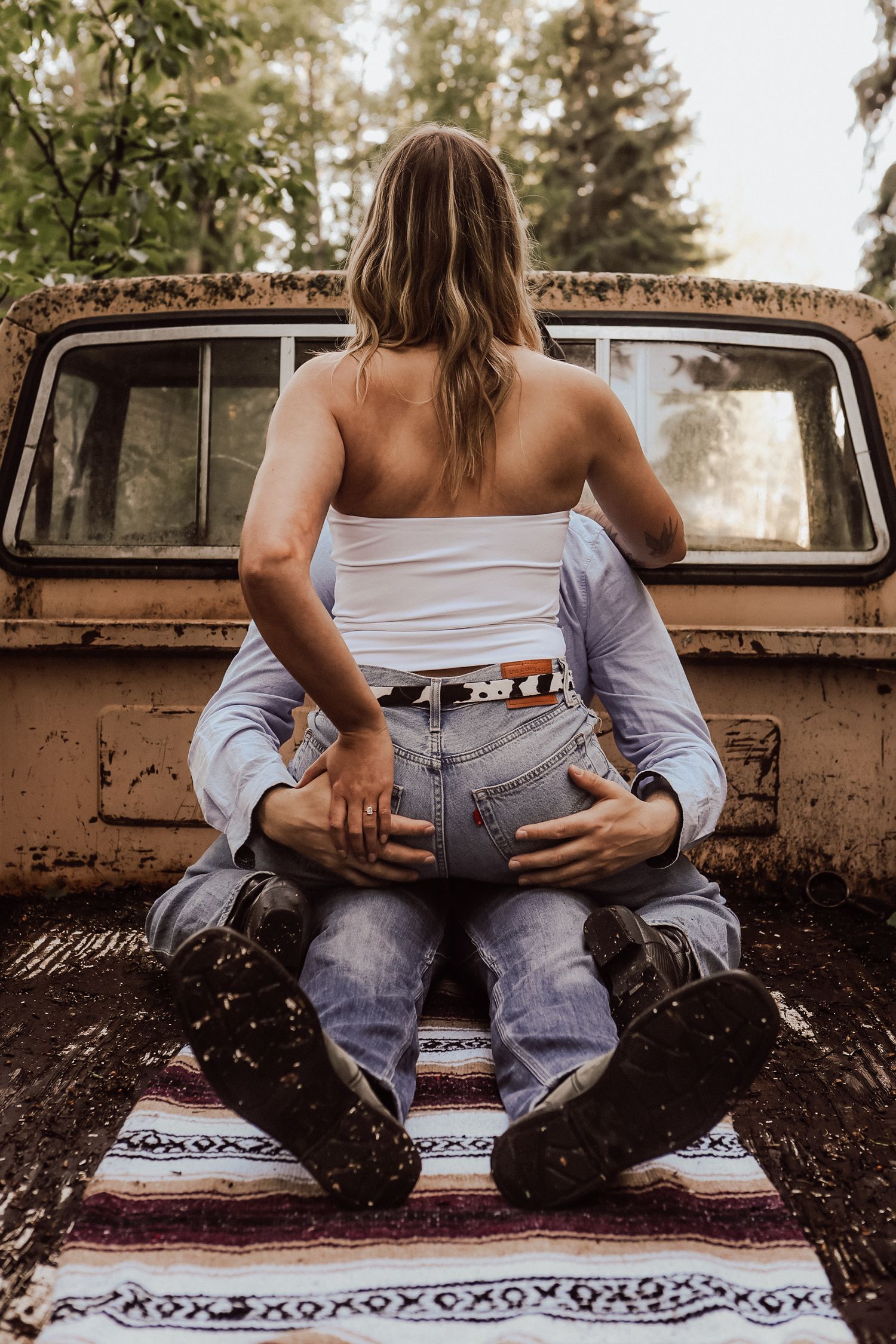 Couple sharing an intimate moment on a vintage truck bed with a bohemian blanket in a forest setting.