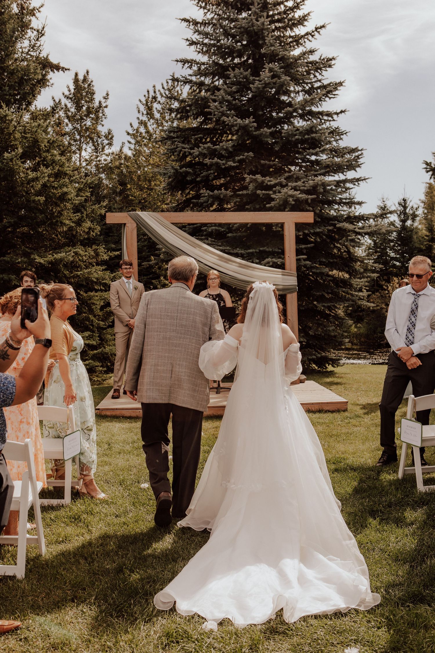Emotional first look wedding ceremony sequence in an outdoor garden setting with wooden arch and evergreen trees.