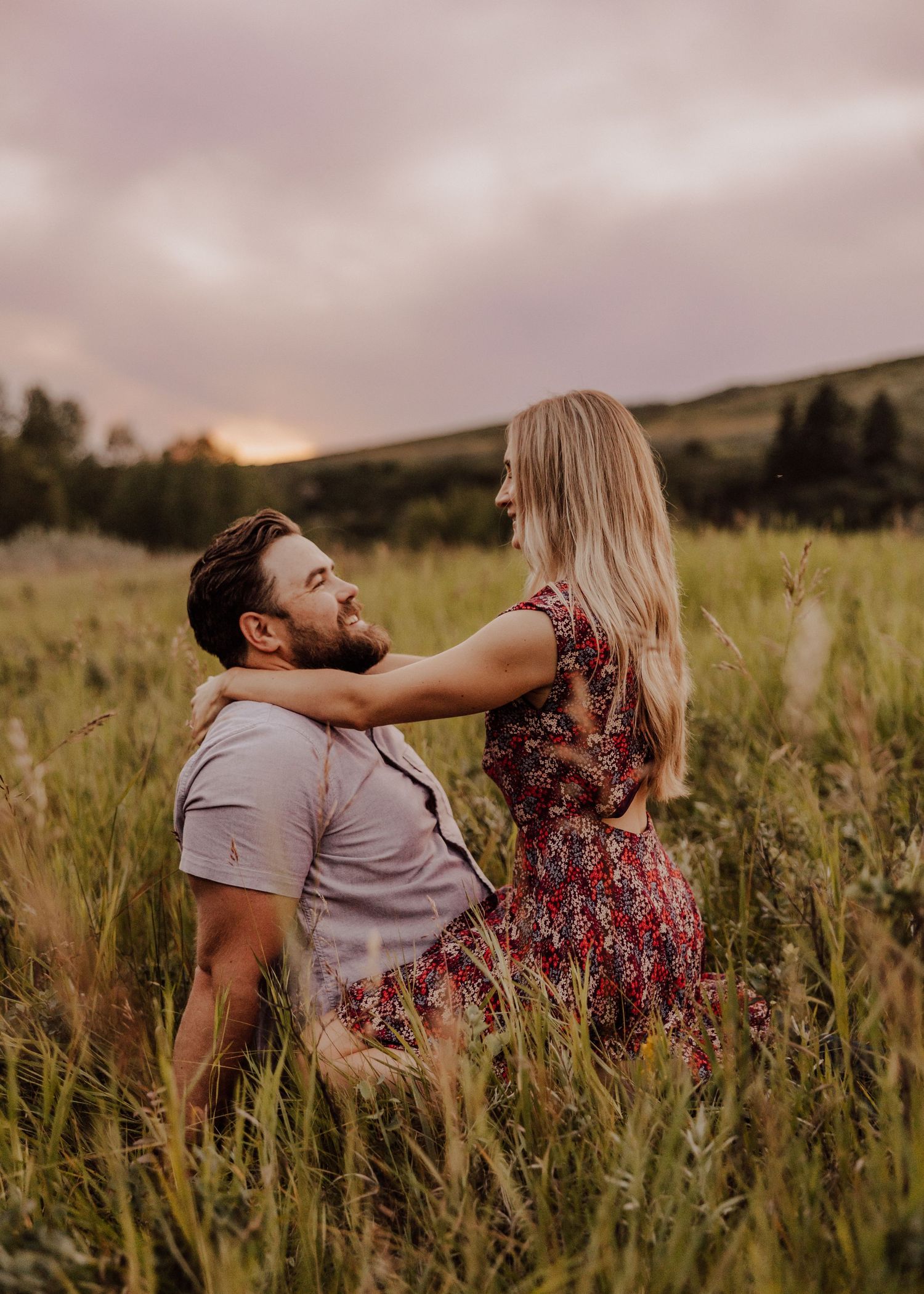 A couple embraces in a golden field at sunset with rolling hills in the background.
