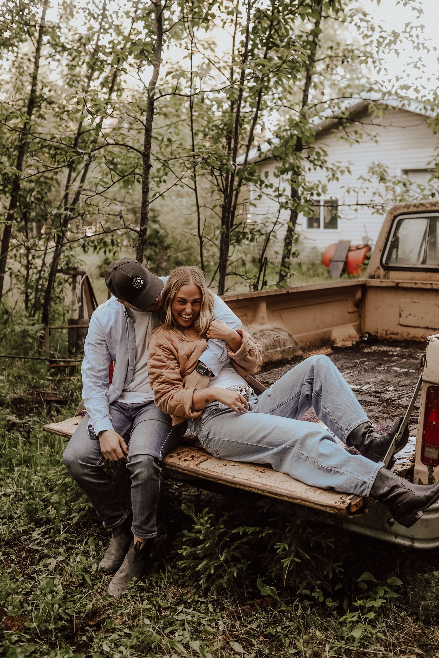 Couple relaxing together on the back of a rustic brown pickup truck surrounded by trees.