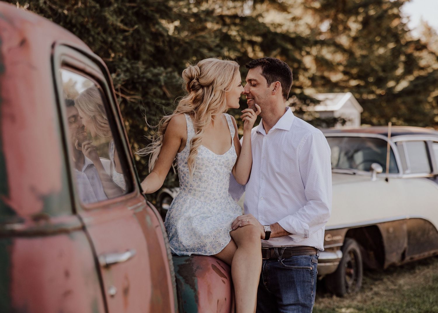 Couple sharing a romantic moment leaning against a vintage rusty truck outdoors during golden hour.