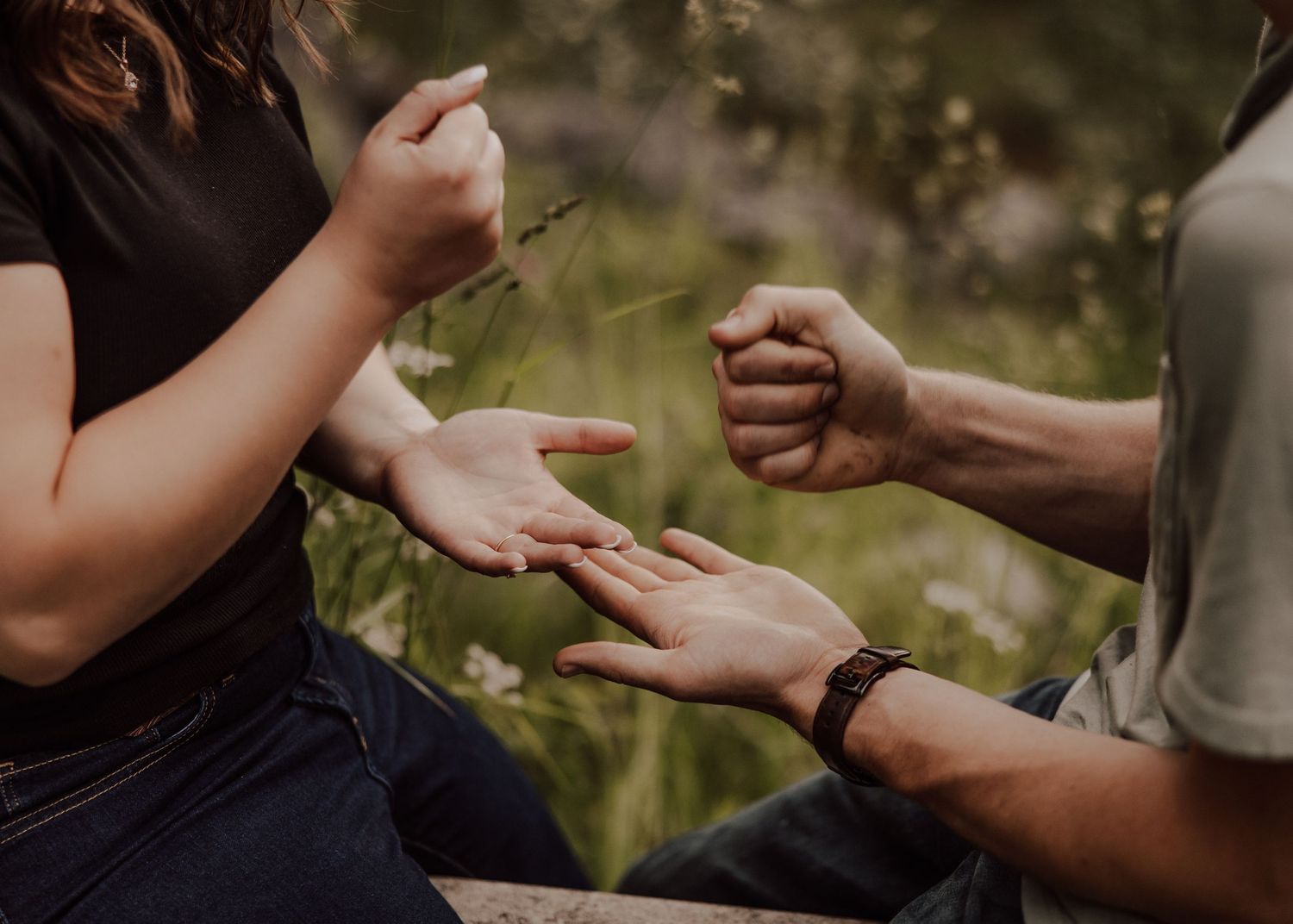 Close-up shot of hands holding each other in a natural outdoor setting with sunlight and greenery in the background.