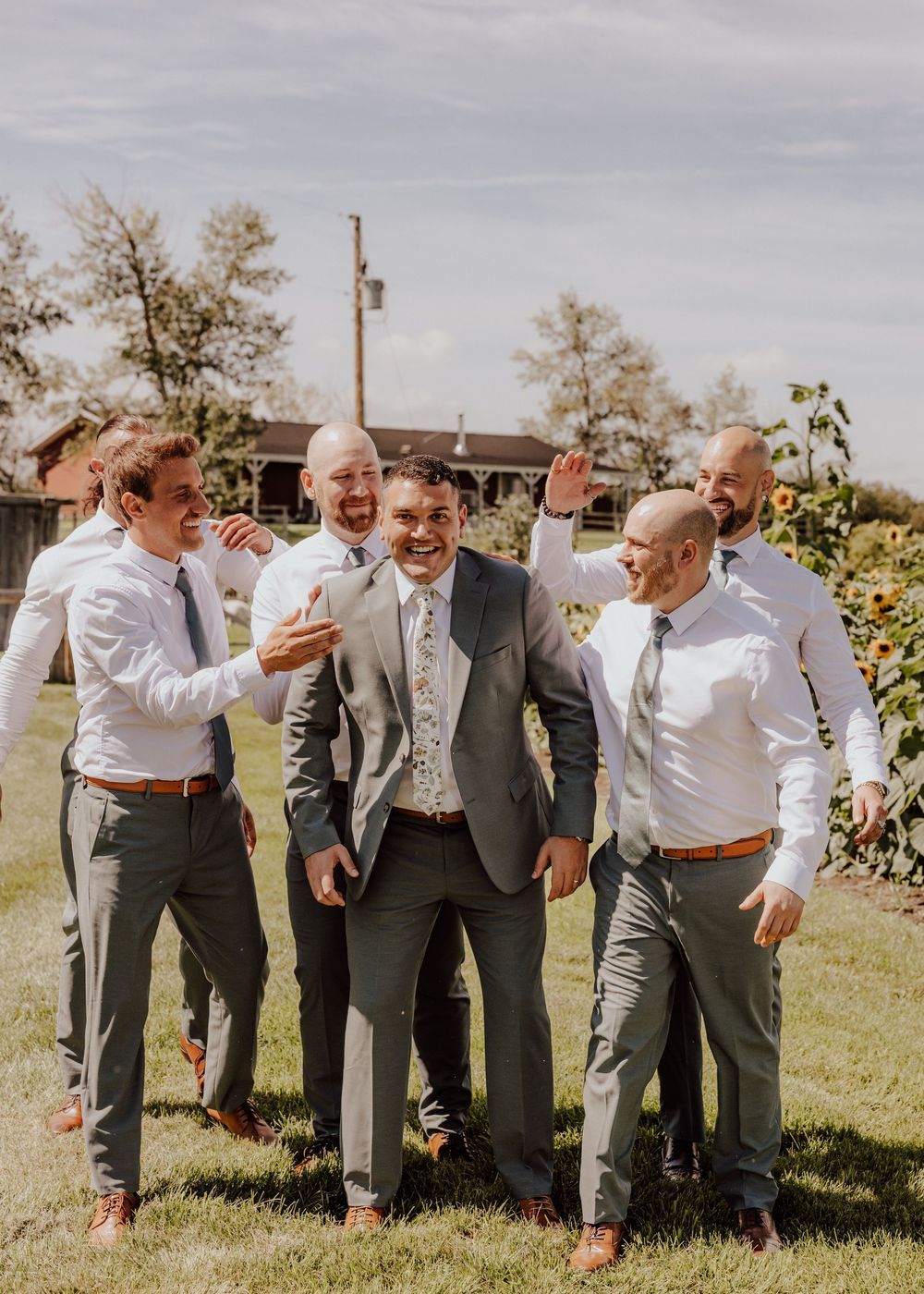 Groomsmen in grey suits share laughs during casual outdoor wedding photo session.