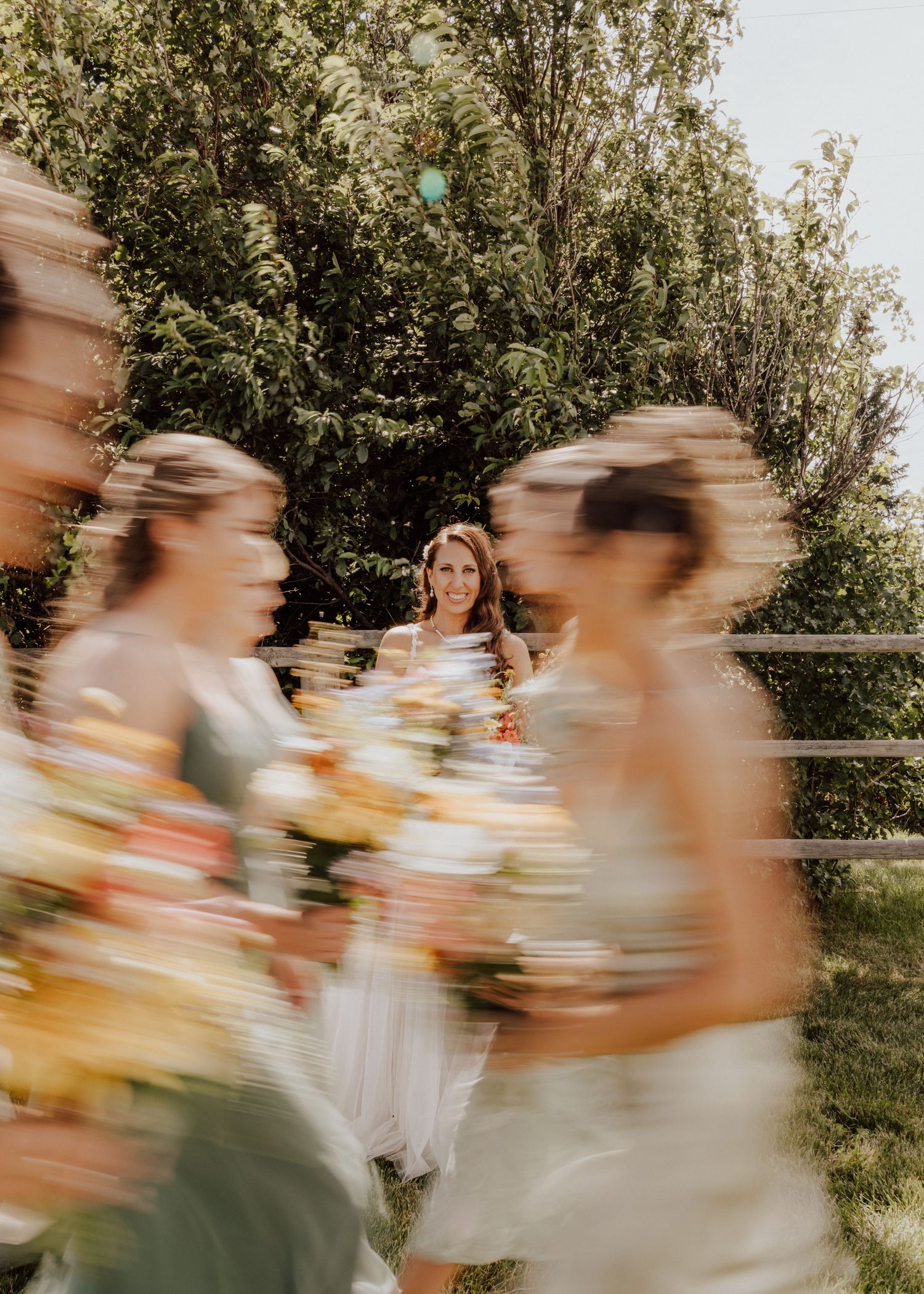 Motion-blurred wedding party walking in a line creates an artistic effect against green foliage.