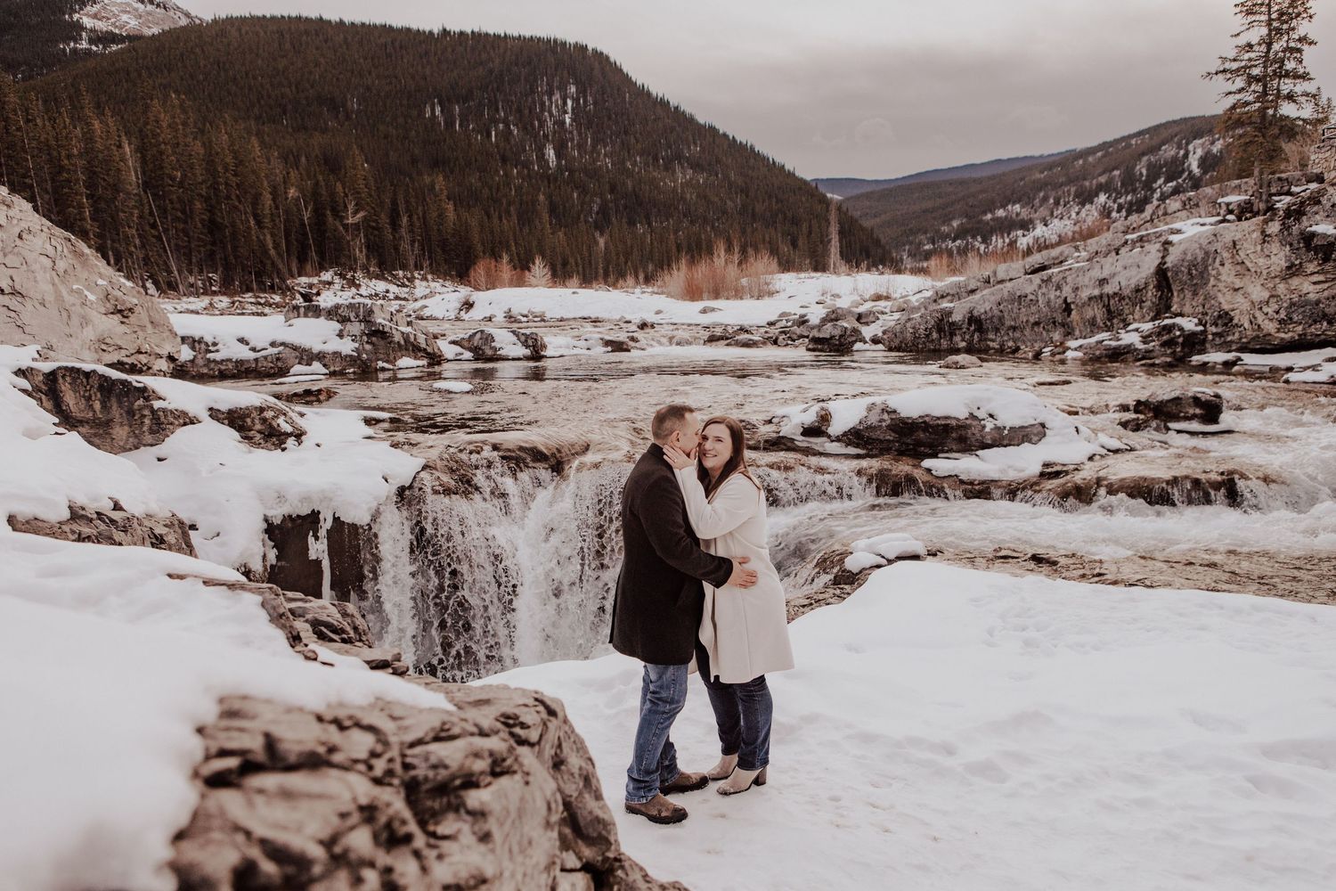 A scenic winter engagement photo session shows a couple in warm coats walking through snowy mountain landscapes.