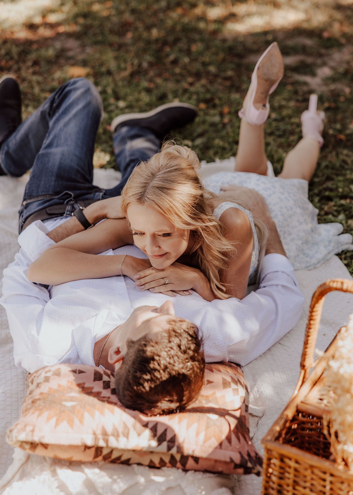 Couple enjoying a romantic outdoor picnic on a blanket, woman lying on man with wicker basket nearby.