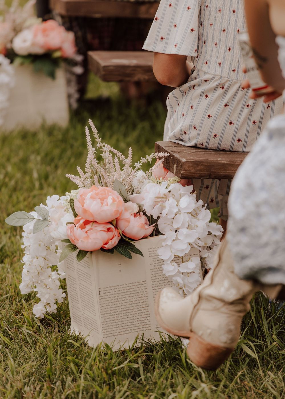 Decorative floral arrangements in vintage books displayed on grass at outdoor wedding.