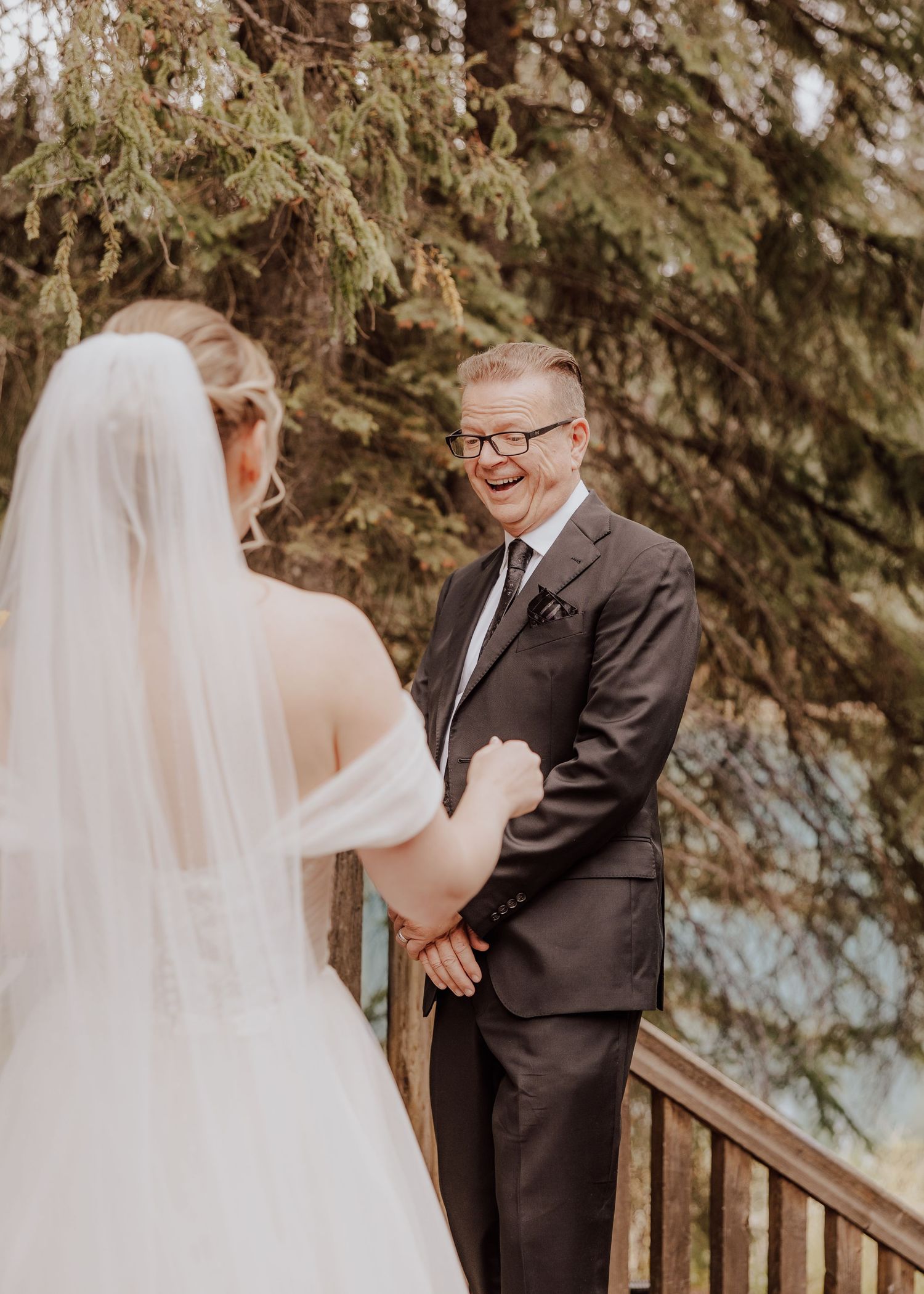 An emotional first look moment between a bride in white and a gentleman in a dark suit on outdoor wooden stairs.