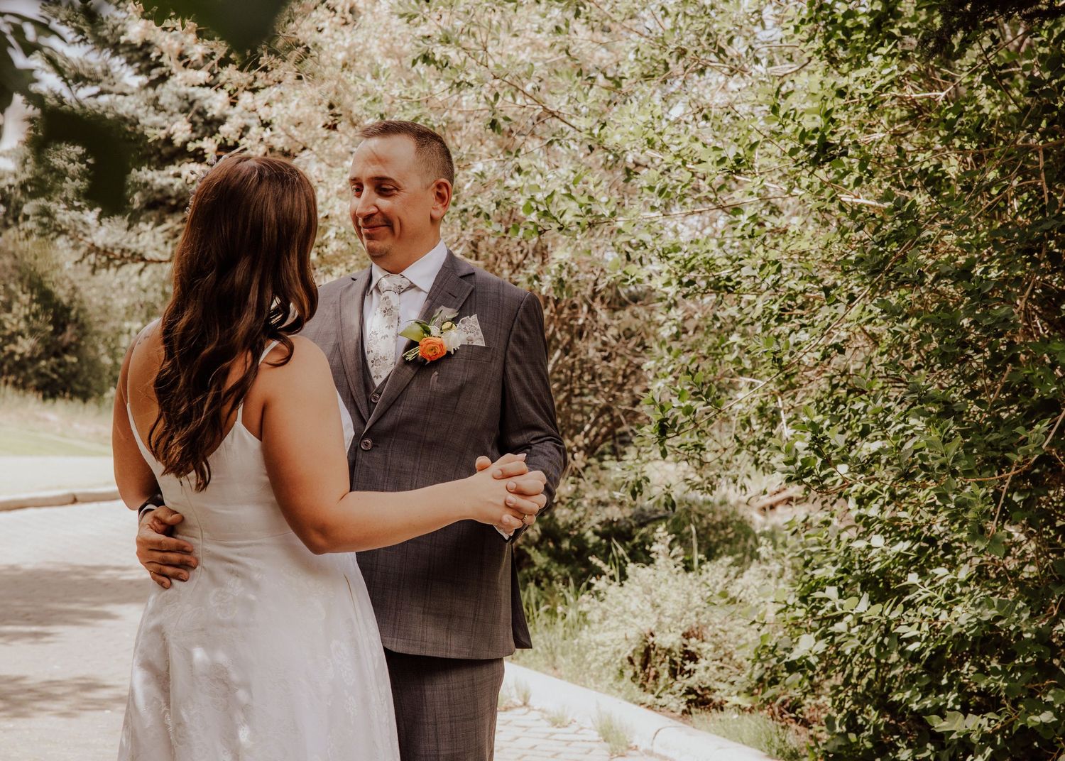 A couple shares an intimate moment outdoors in a sunlit garden setting during a wedding celebration.