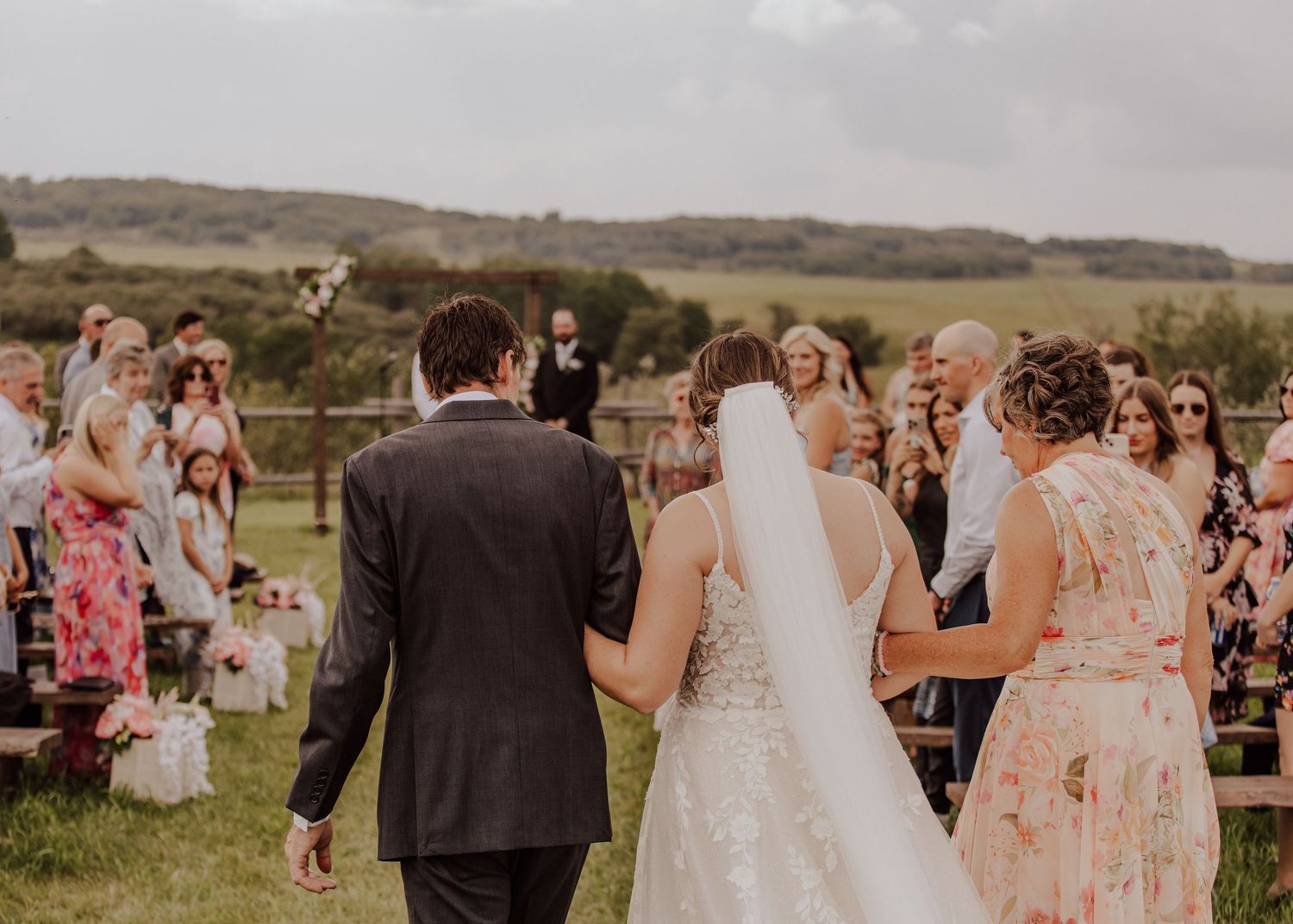 Wedding guests mingle and celebrate on a scenic hillside during an outdoor reception at sunset.