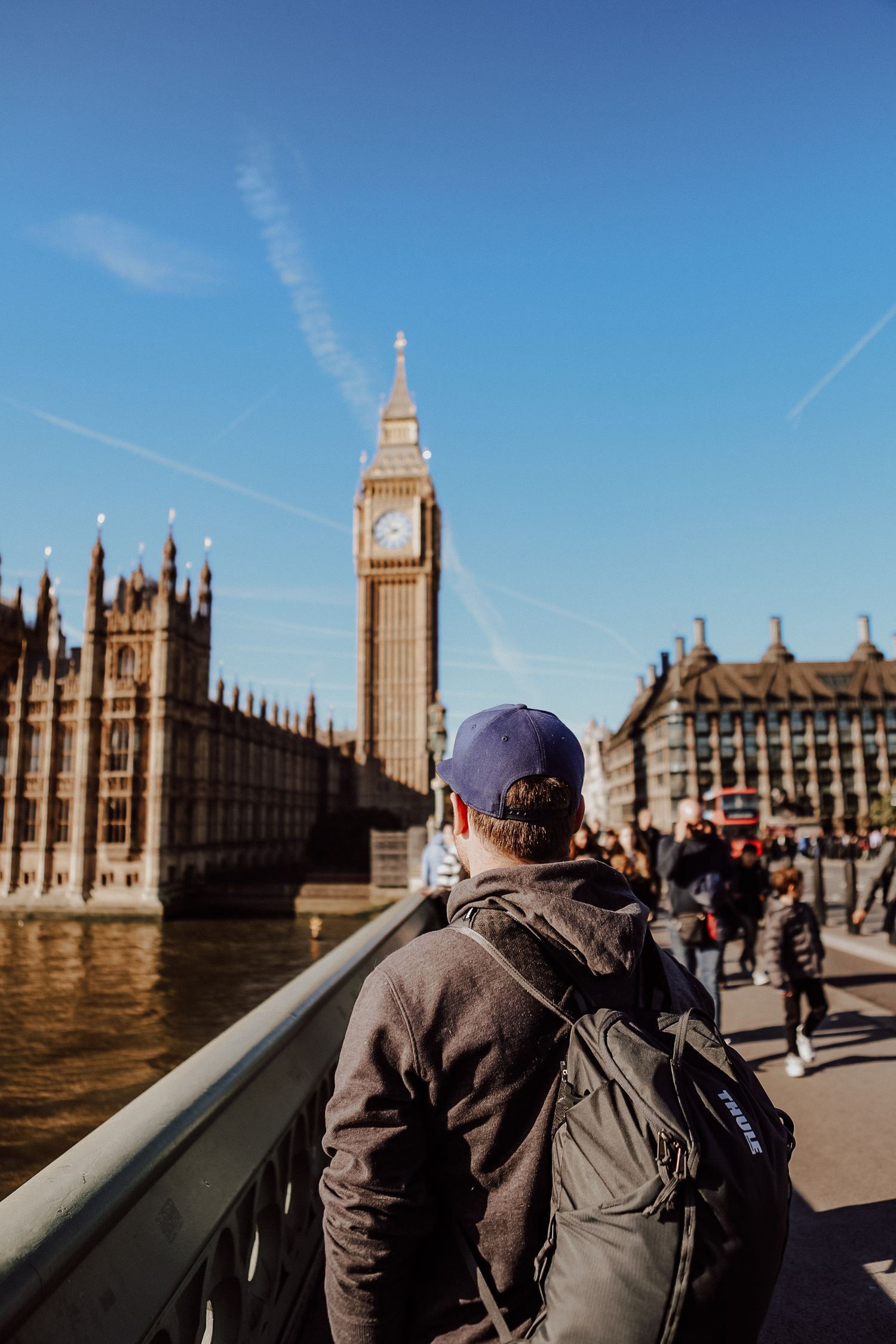 Tourists admiring the iconic Houses of Parliament building in London against clear blue sky.